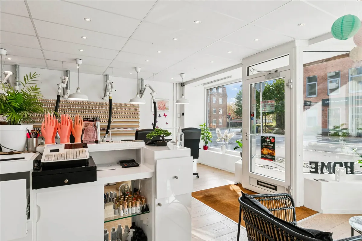 Hvid indretning med høj gulvbelægning og lysekroner med skumle lys. På højre side er en indgang med skrift og plante i