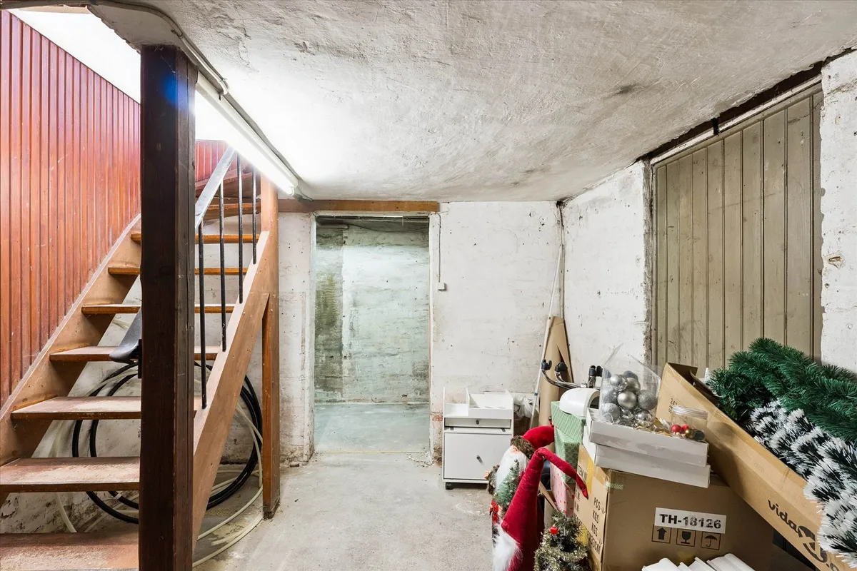 Kælder med trappe, lagerkasser, juletræsdekorationer og hvidt vægmaleri