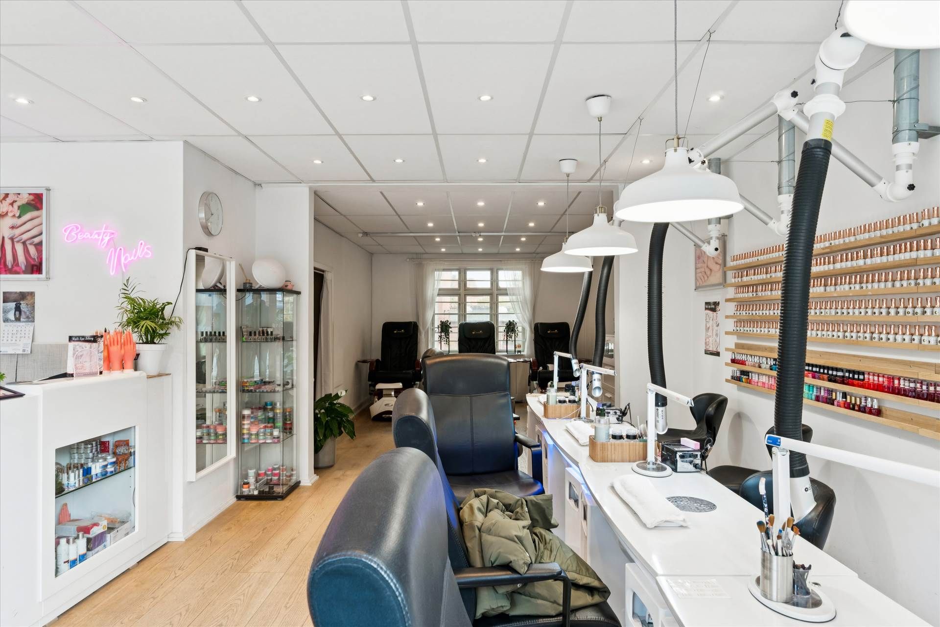 En moderne og pæn indretning med høje lofter, lyse gulve og lysekroner med hvide lampeskærme. Der er stolpeformet