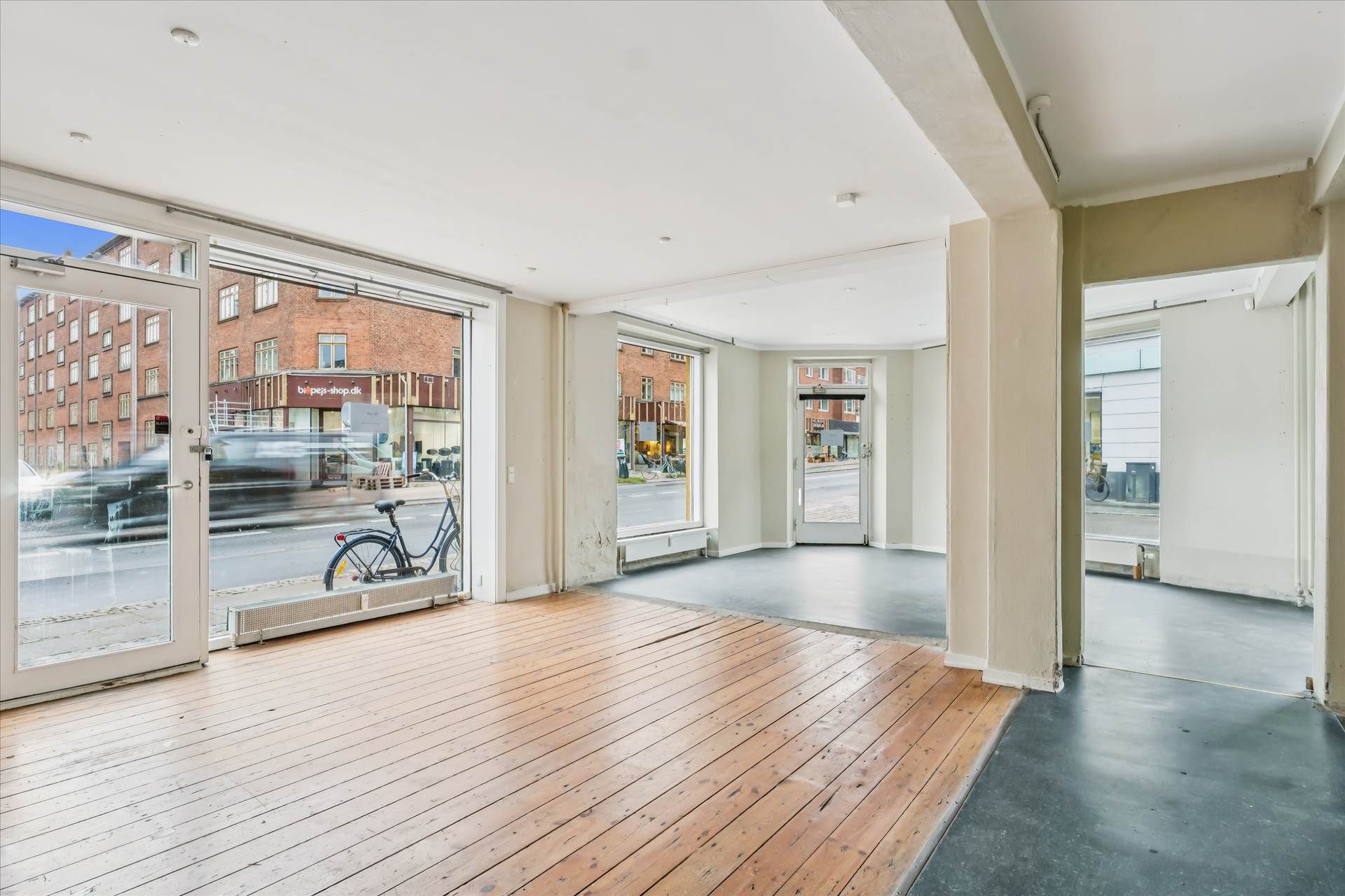 Indvendigt billede af hjørnebutik med glasdøre, lyse gulve og store vinduer ud mod gågade og biler