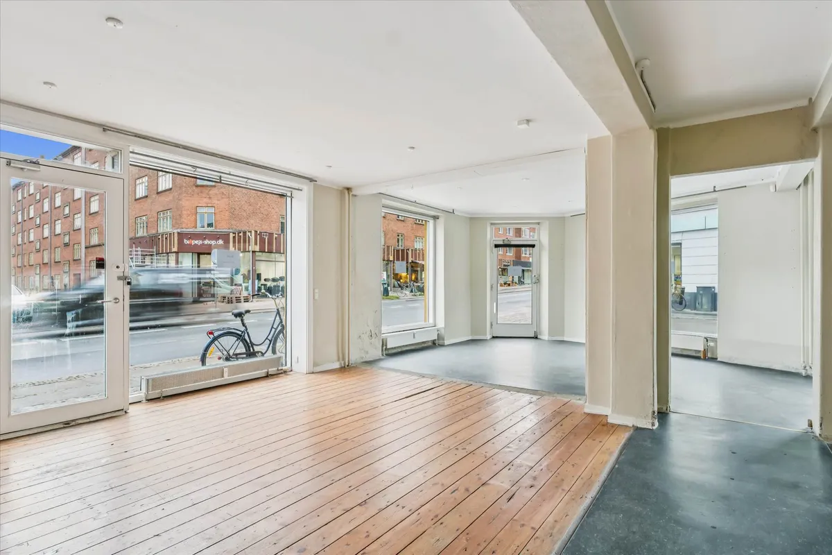 Indvendigt billede af hjørnebutik med glasdøre, lyse gulve og store vinduer ud mod gågade og biler