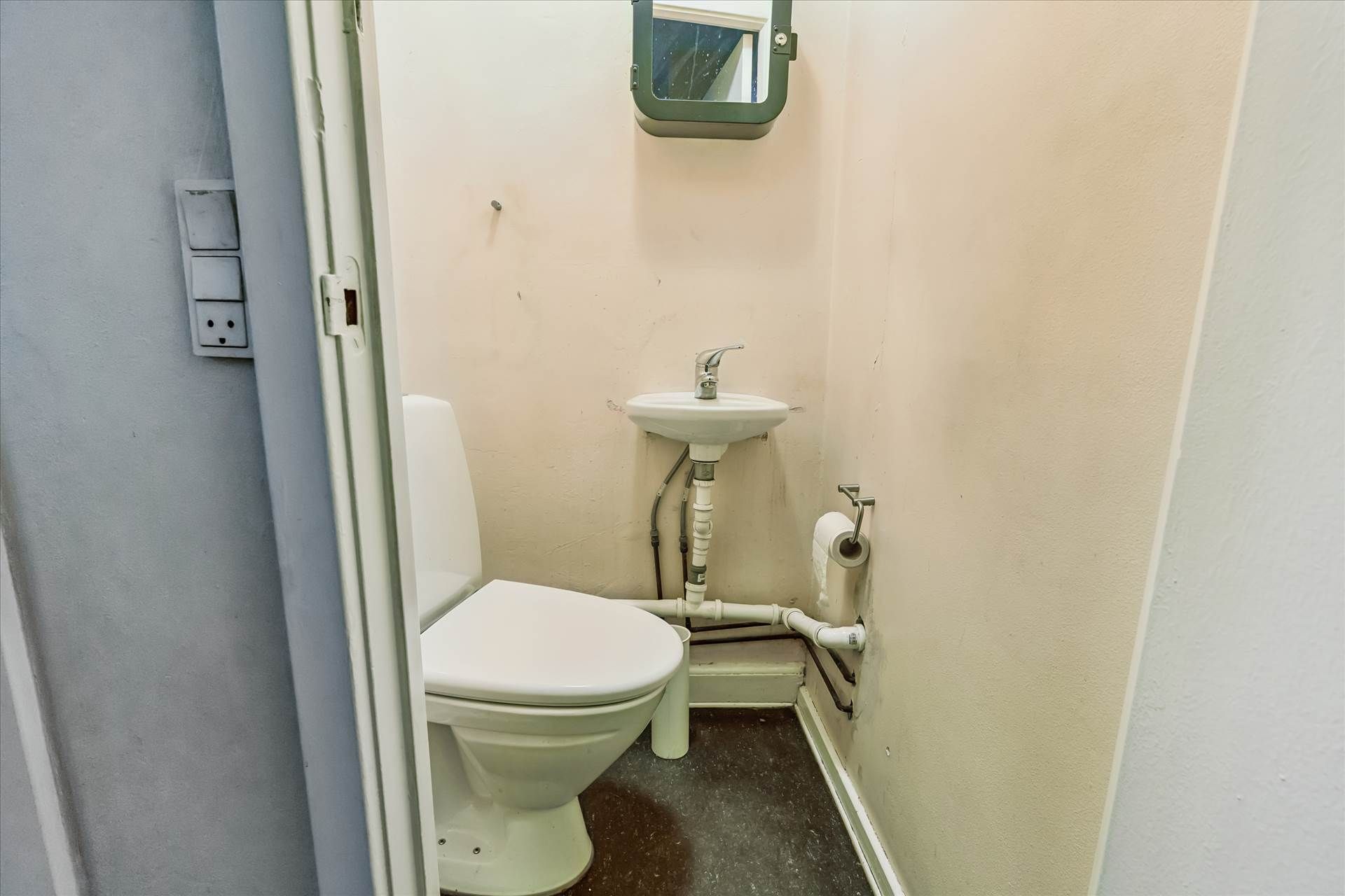 Toiletrum med hvid toilet, hvidt vask og tøjholder til håndklæde. Der er også en stribet spejl og elektriske stik.