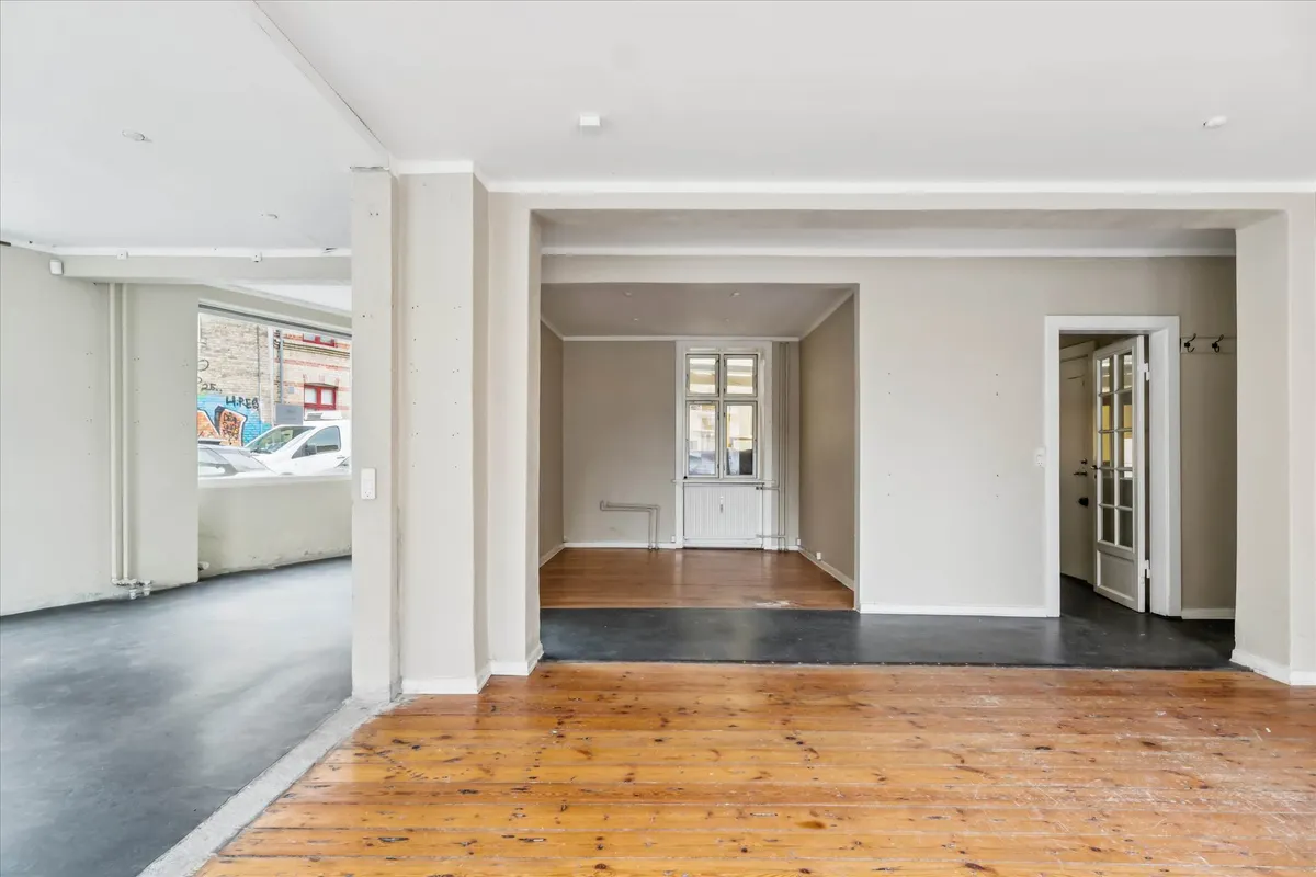 En stor og mørk hjørnebutik med lysegul og hvid vægbeklædning samt trægulve og en dør til et lagerrum