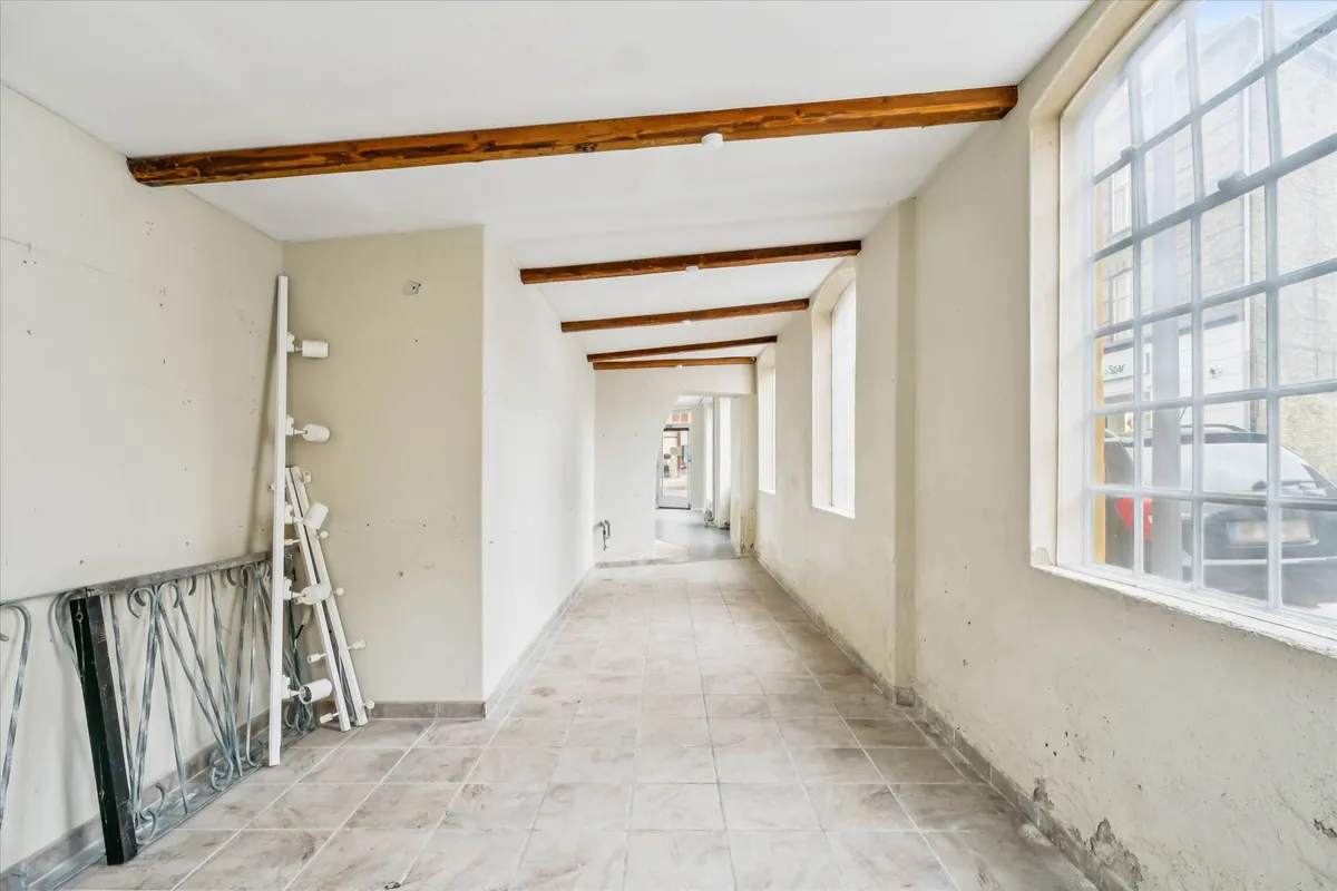 Køkken med lyse gulvfliser og lysegrå vægge, der vender mod en gård med parkerede biler og vinduer i baggrunden