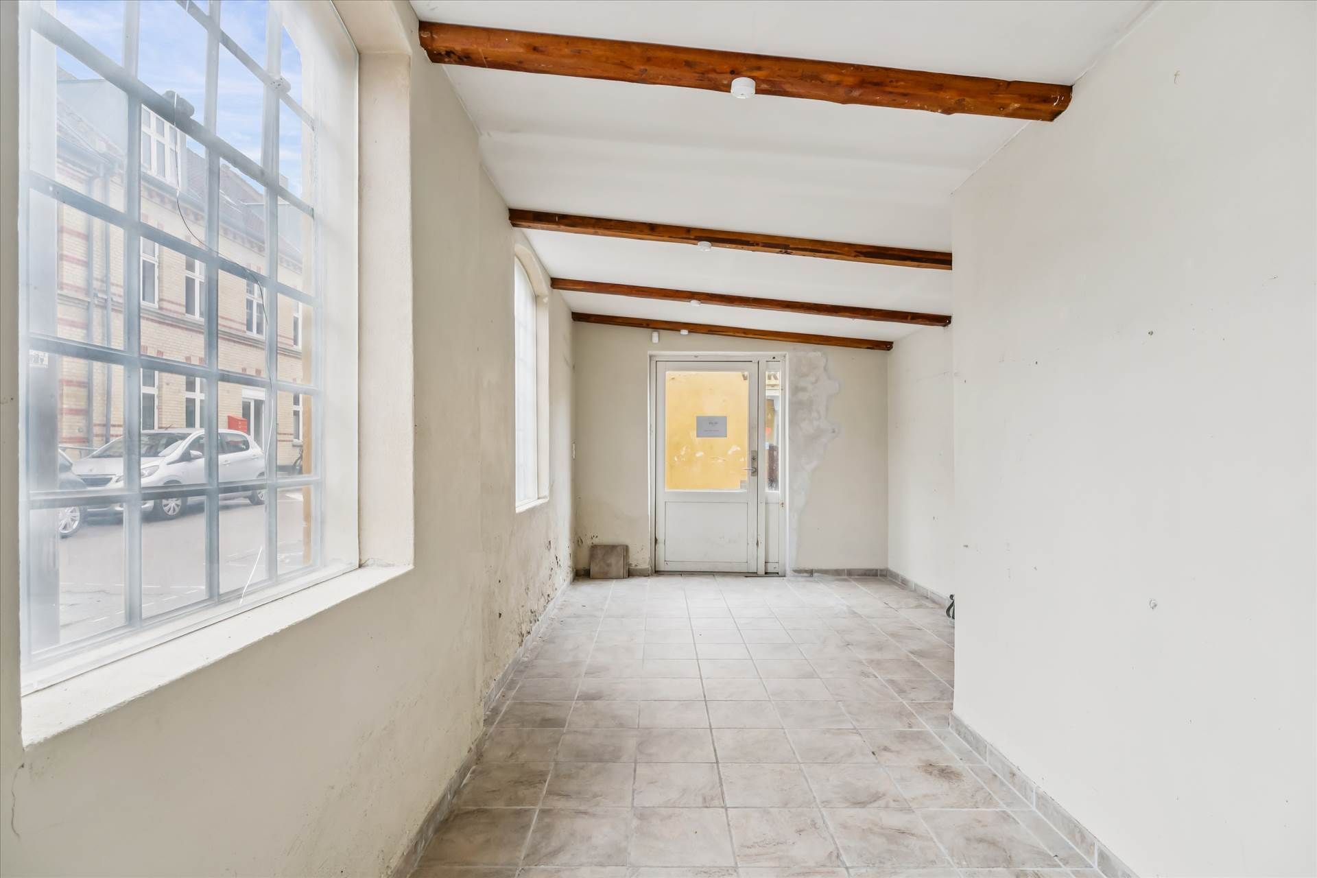 En tomt hjørnelokale med store ruder og træloft i Valby med en hvid dør og gulv af gulfliser