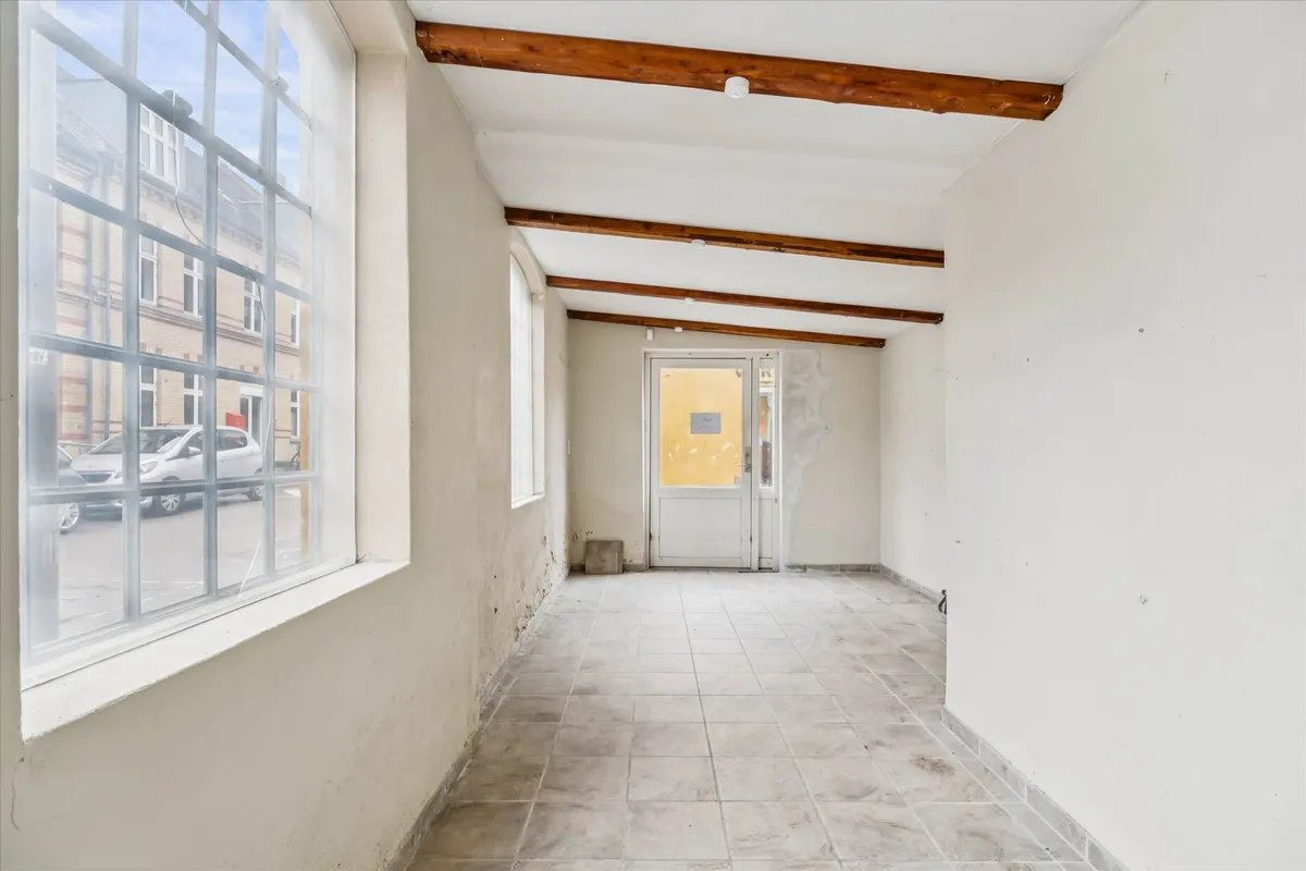 En tomt hjørnelokale med store ruder og træloft i Valby med en hvid dør og gulv af gulfliser