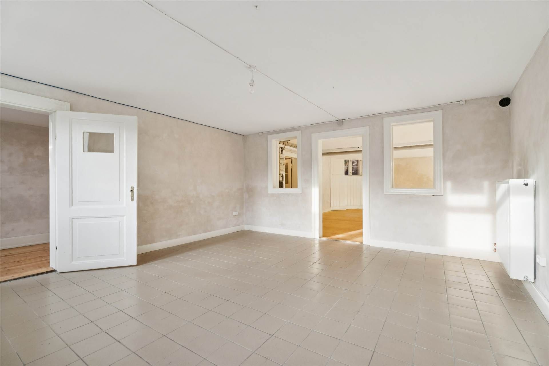 Hvidt rum med hvide vægge og gulvtæppe, hvide døre, en hvid radiator og vinduer med hvide omrammer