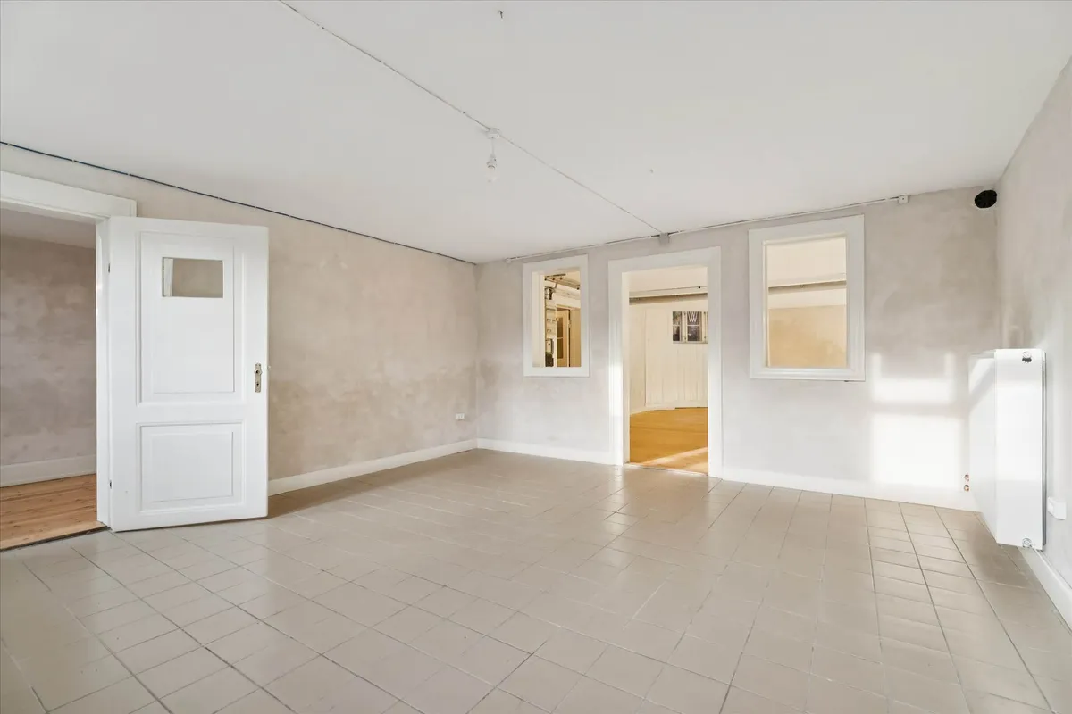 Hvidt rum med hvide vægge og gulvtæppe, hvide døre, en hvid radiator og vinduer med hvide omrammer