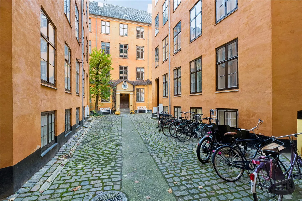 En smuk gammel bygning i Frederiksstaden med flere cykler parkeret udenfor og en lille have med bænke