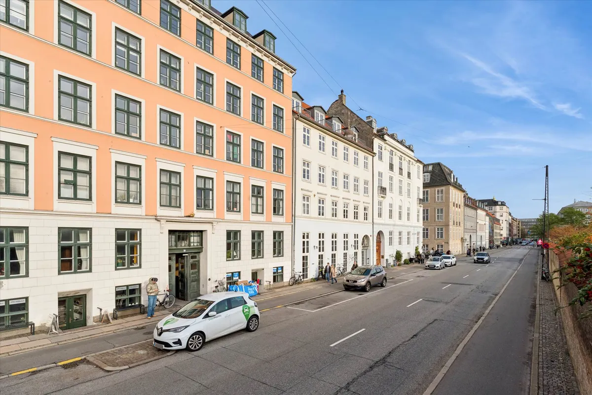 En bilparkeret på en gade i en by. På højre side er en bygning med flere biler parkeret. På venstre side er en person med en