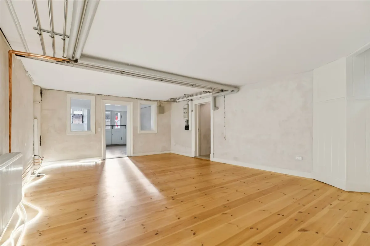 En stor tom rum med lysegult trægulv og hvide vægge samt lysekroner og radiatorer i det ene hjørne