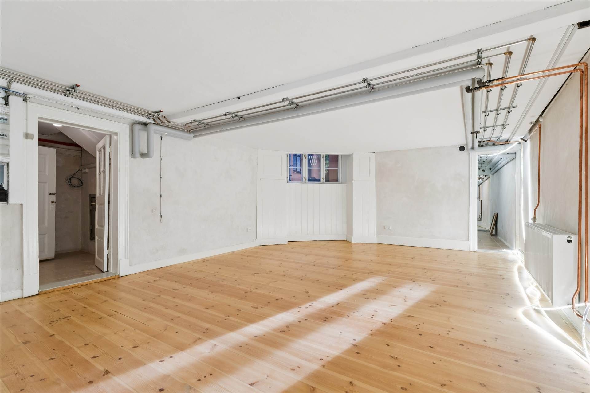 Lyst og pænt kontor med lyse lofter og højt til loftet, hvide vægge, lyse trægulve og køkken med moderne apparater