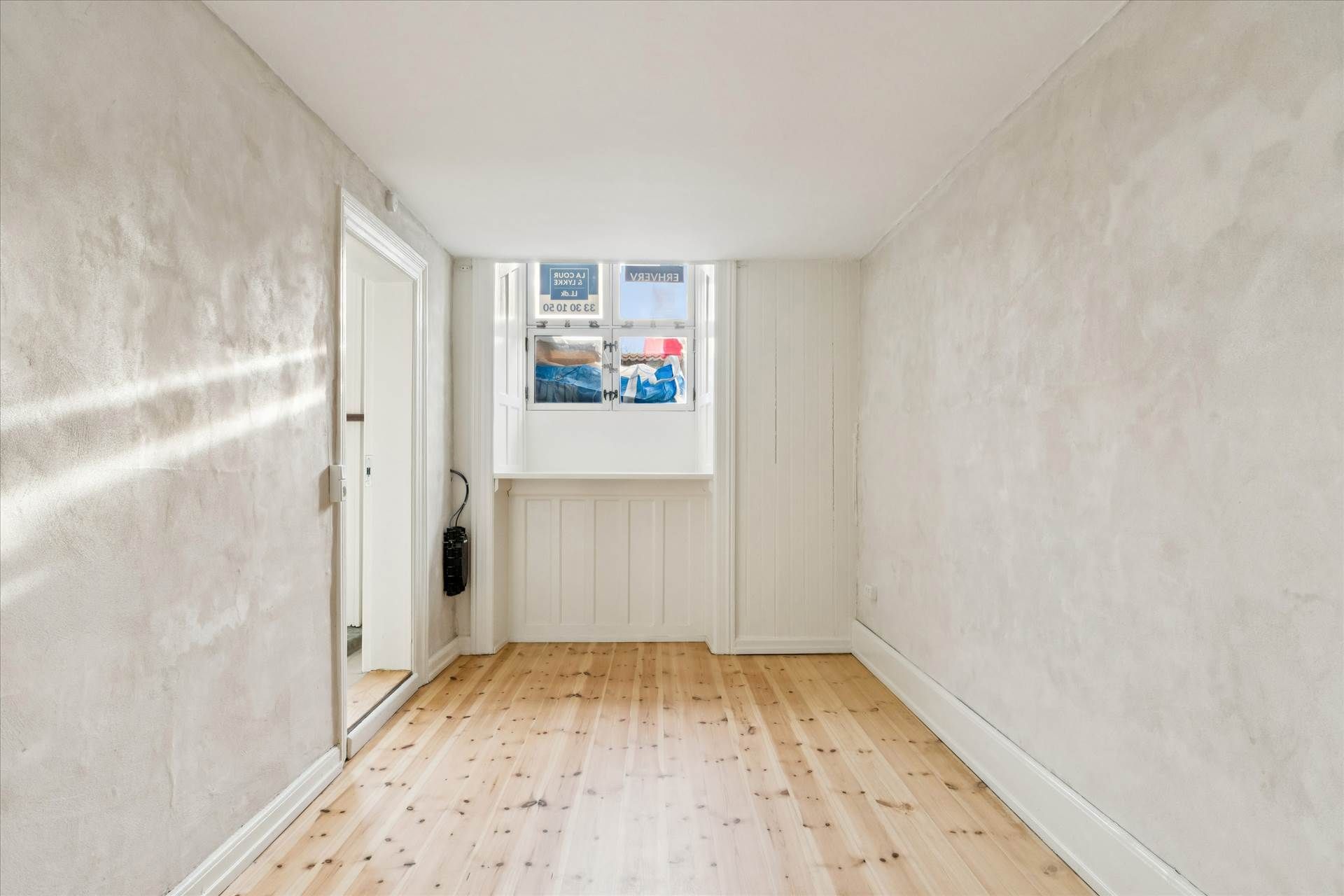 En tom og lys hal med hvidt loft og gult gulv og to døre samt et vindue med tekst og emballage i det