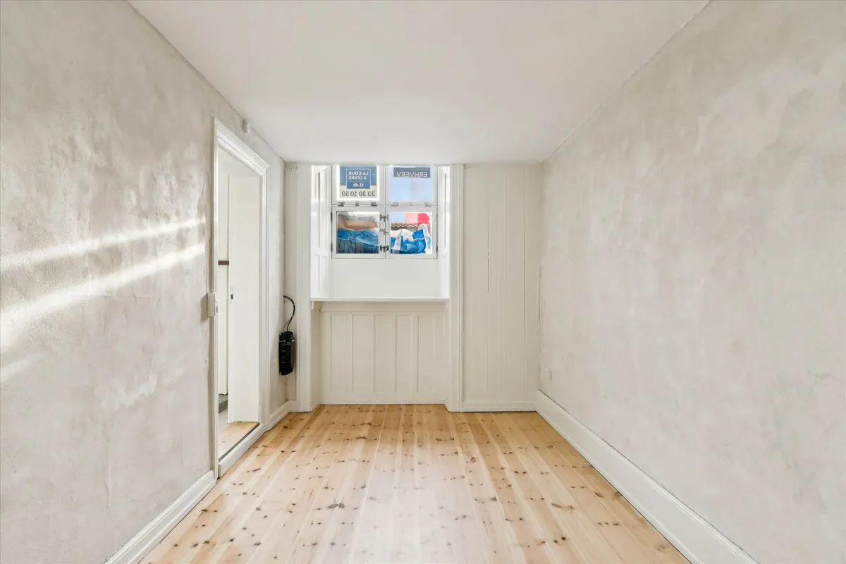 En tom og lys hal med hvidt loft og gult gulv og to døre samt et vindue med tekst og emballage i det