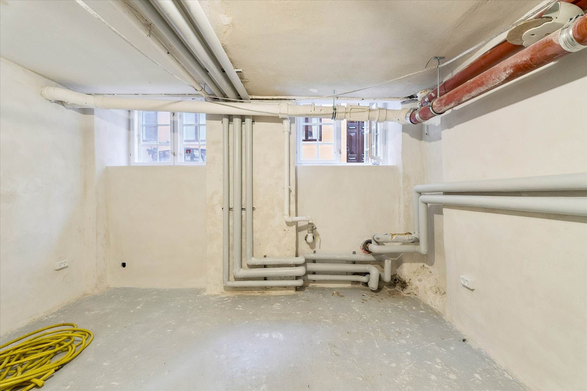 Et stort og velholdt rum med mange hvide rør og en gul slange på gulvet