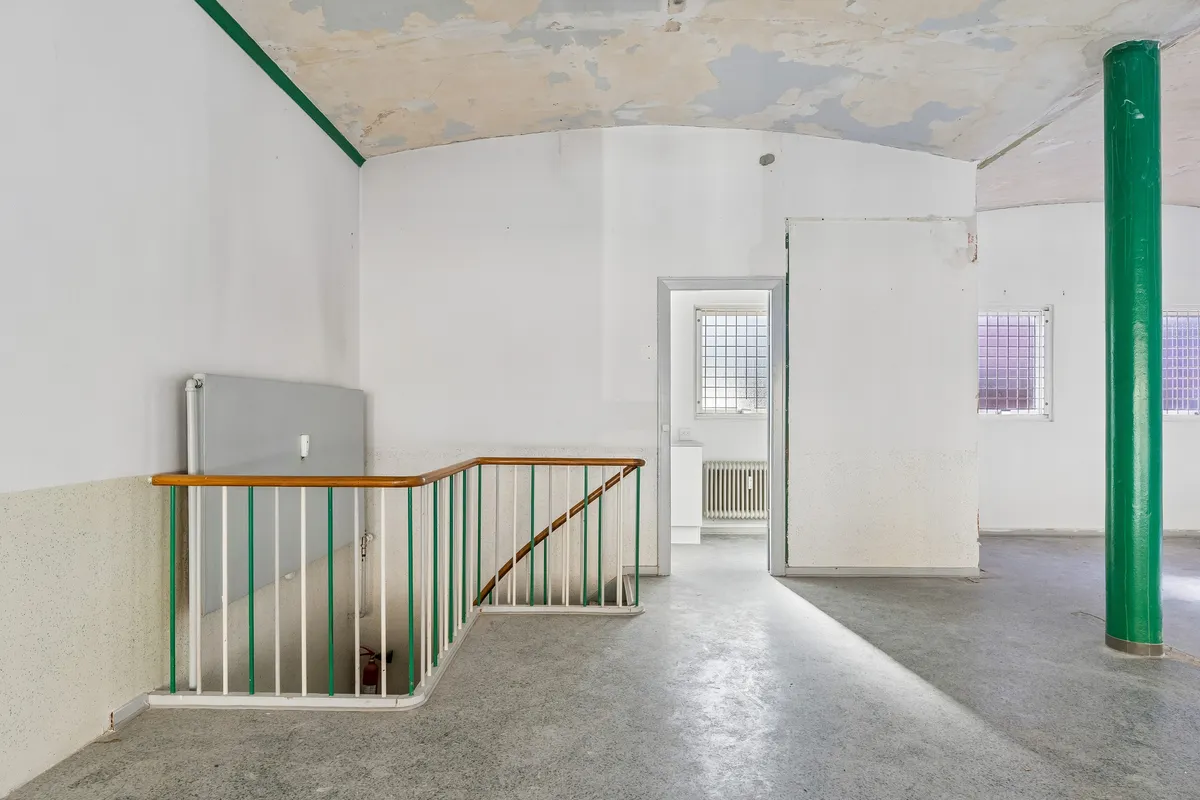 Kontorlokation i Frederiksberg med lyse og rummelige værelser, hvid maleri, grøn søjle og moderne trappe.