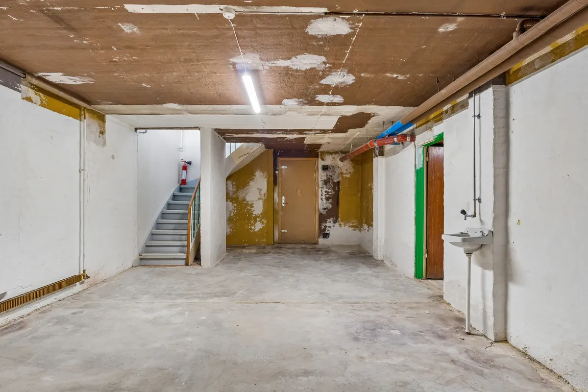 Foto af en mørk og rummelig lagerhal med lysegul gulvbelægning, højt loft, trapper og en vandhane i hjørnet