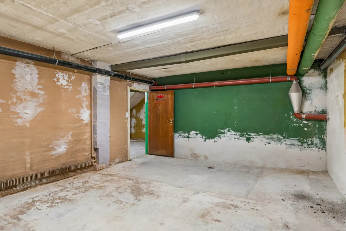 Kælder til leje med lyse og høje lofter og lyse skilte på døren og på væggen med røde og grønne farver og lyse ledlys i loftet