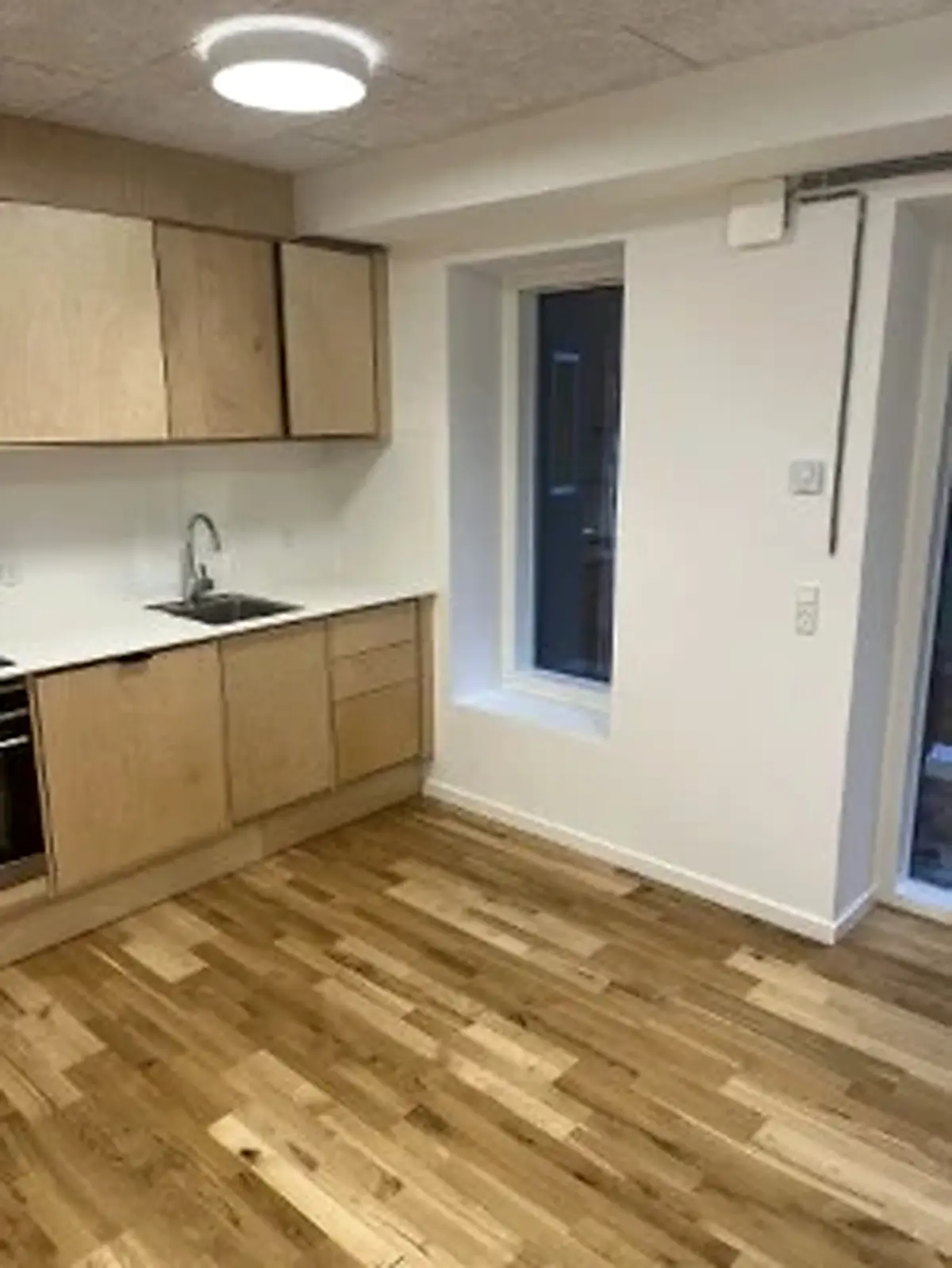 Kontorlokale med eget køkken og badrum. Rent og pænt køkken med lyse træskabe, hvidt arbejdstræk og gulvbelægning. Vindue med glas og træindfatning.