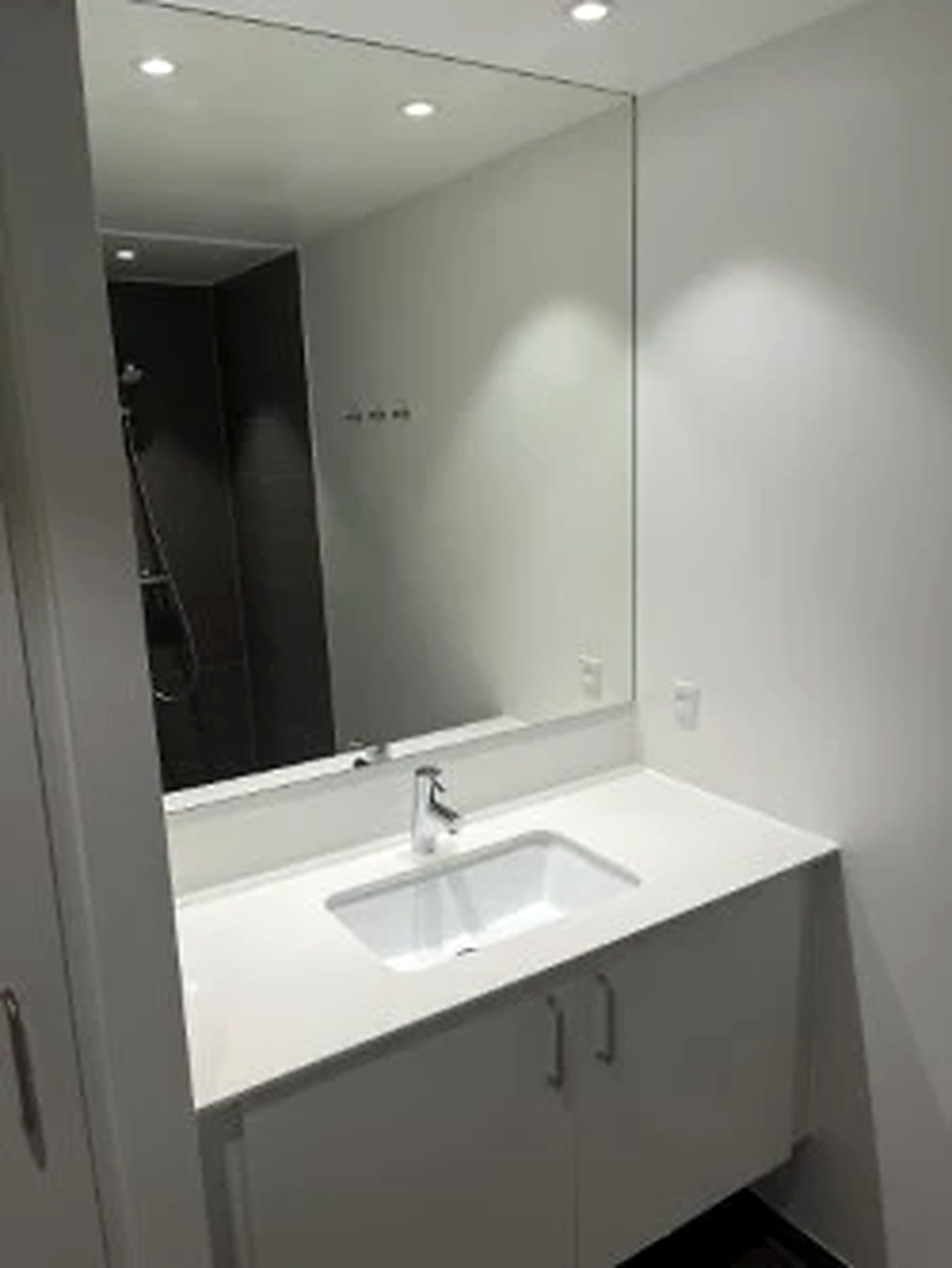 Bad med stor spejl og hvidt badeværelsesskab med vandhane. Højloftet badeværelse med lyse og moderne design. Hvidt skab og spejl giver ekstra plads og komfort.