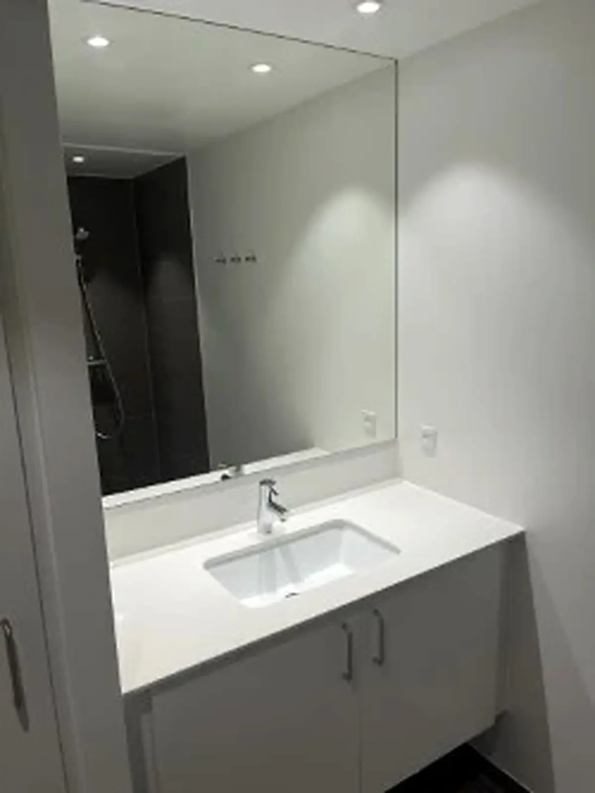 Bad med stor spejl og hvidt badeværelsesskab med vandhane. Højloftet badeværelse med lyse og moderne design. Hvidt skab og spejl giver ekstra plads og komfort.