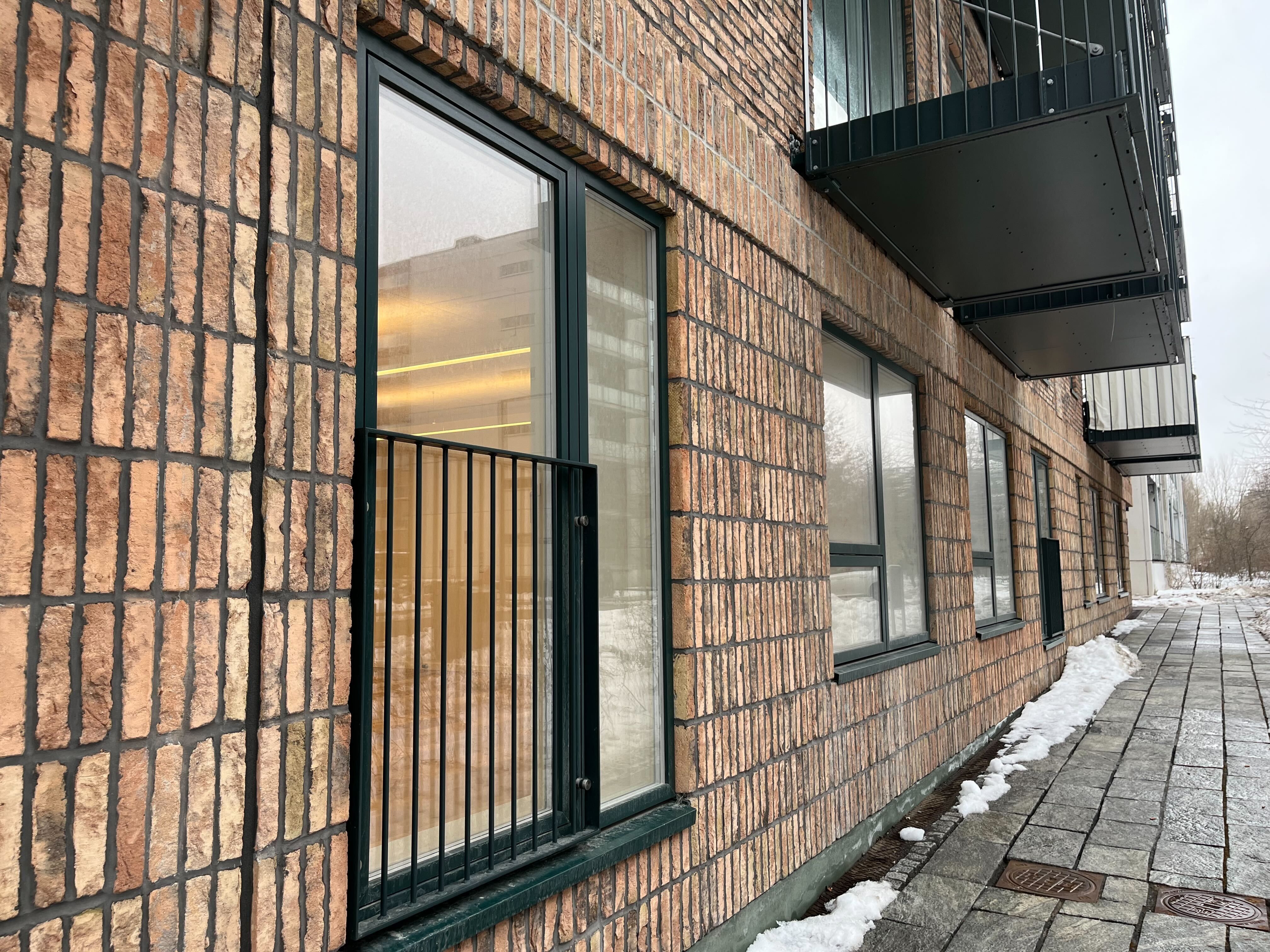 Lyst og funktionelt kontorlokale med eget køkken og bad. Murstens facade og vinduesruder i grønt. Balkon med metalgitter og et snedækket område til siden.