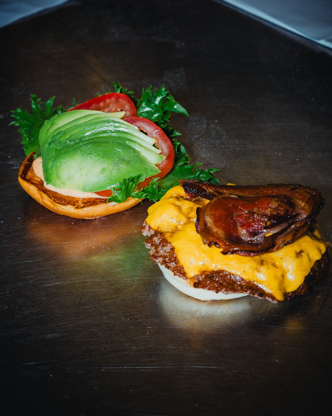 To hamburgere på rustfrit stål servietræ, med bacon og ost på den ene og avocado og tomat på den anden