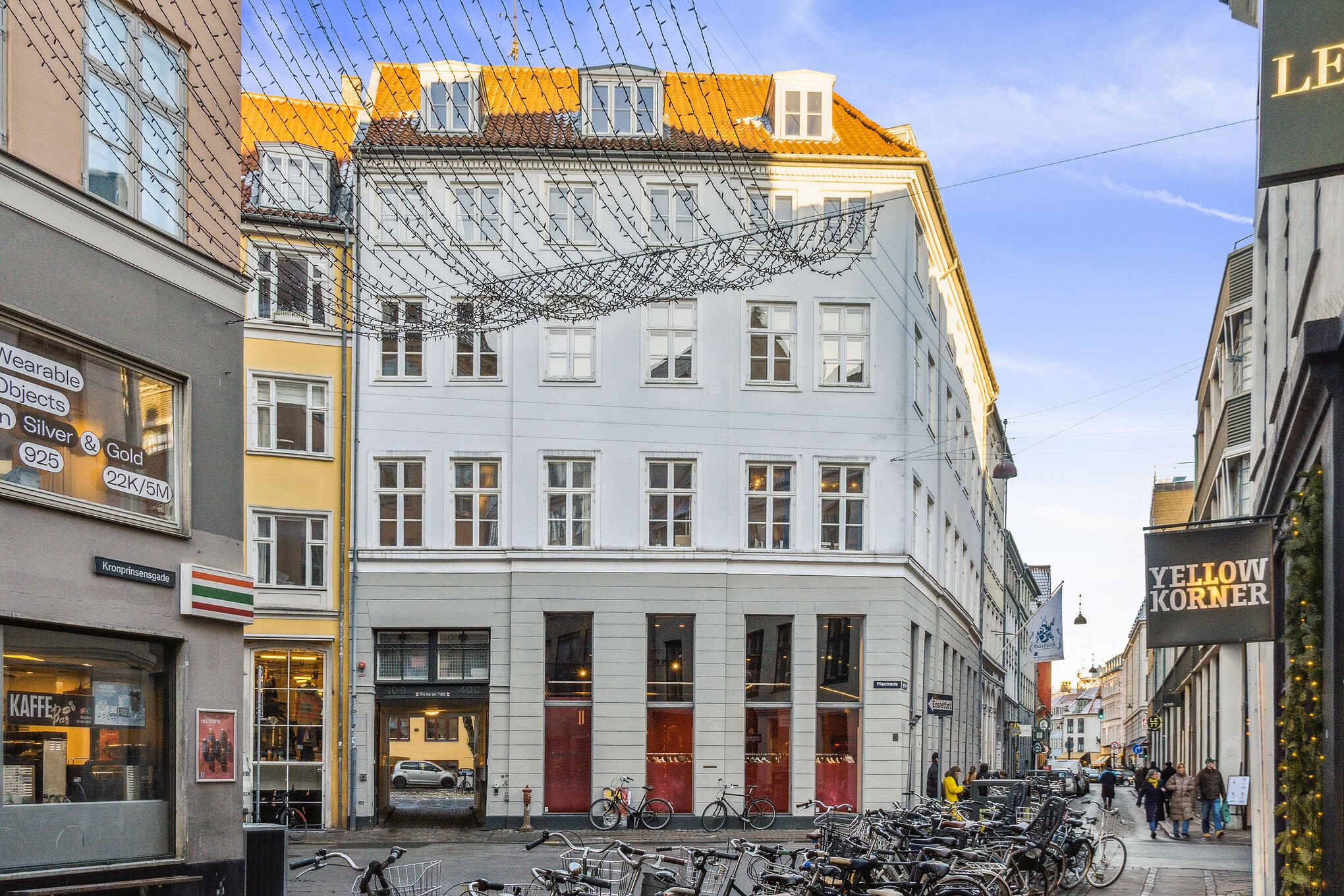Kontor med røde døre på hjørnet af Pilestræde, med mange cykler parkeret udenfor, og udsigt ned ad Kronprinsen. Vægge med lysebue og navnet Yellow Korner
