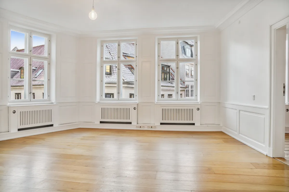 Kontorrum med højt til loftet, lyse gulve og store vinduer med udsigt til byen. Møbler og radiatorer er fjernede og der er to elektriske stikkontakter på væggen.