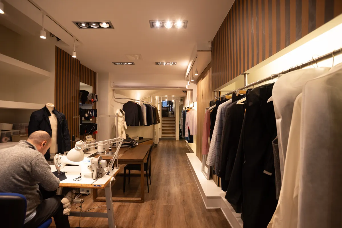 Mænd arbejder i en butik med trægulv og hængende tøj og mænd i jakkesæt og bluser