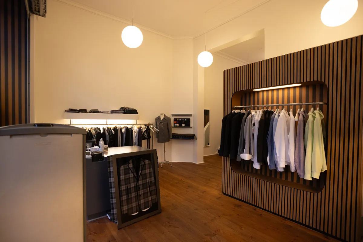 Unik butik med trædekor og moderne møbler, tøjvægge med sort og hvidt tøj, en skraldespand og et salgsbord med et pladebillede