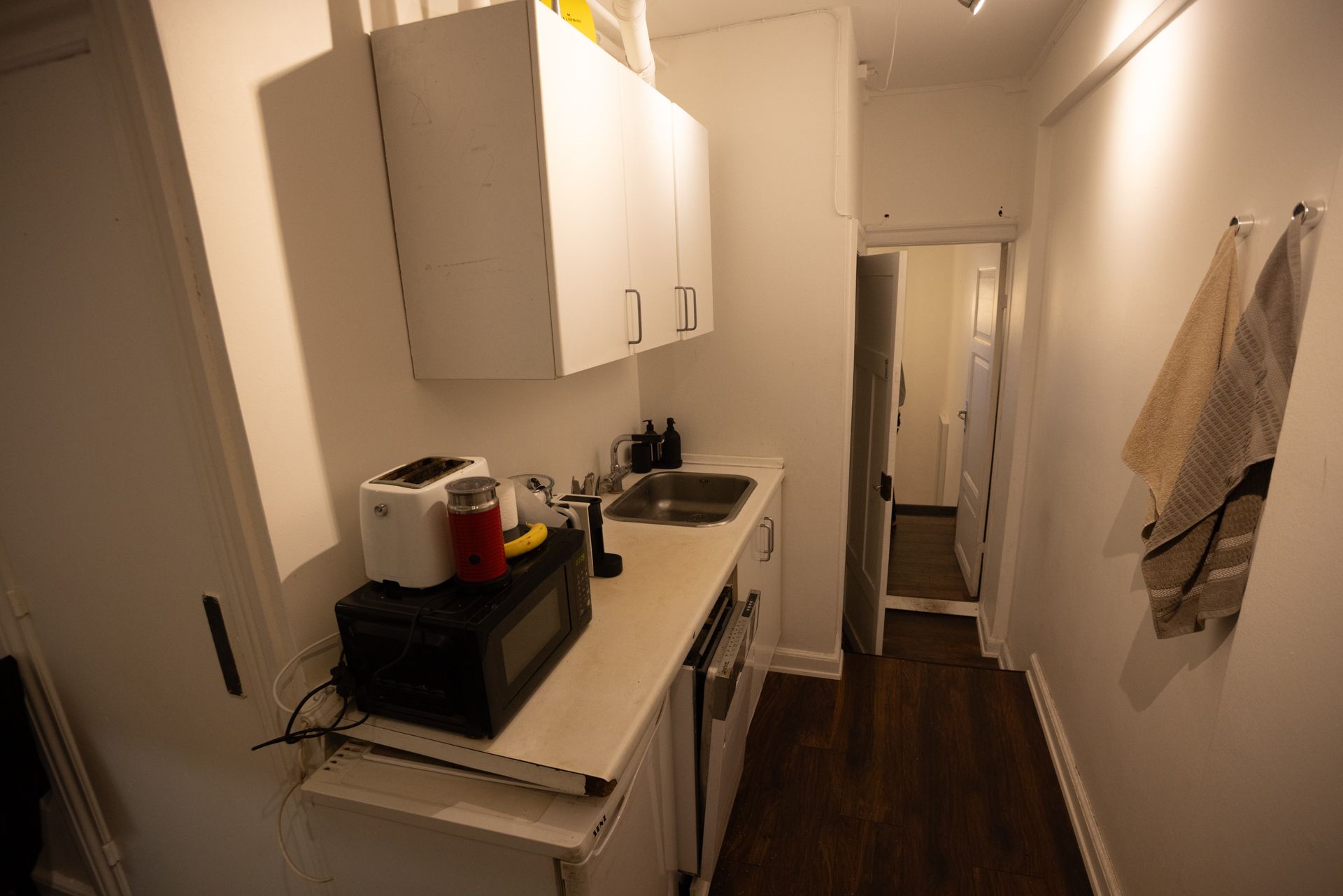 Lejlighedslejlighed i København med køkken med hvidt køkkenskab og to tørklæder hængende på væggen og en indbygget ovn og en mikroovn