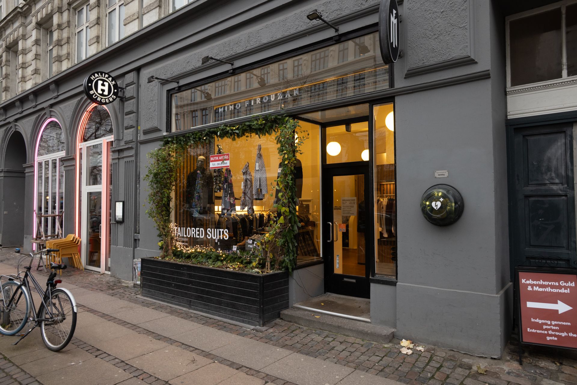 En butiksforretning med navnet HIMO FIROUZAN ligger på Frederiksborggade 37 i København. Der er udsat en plante med forskellige tøj til salg og et skilt med teksten Tailored Suits.