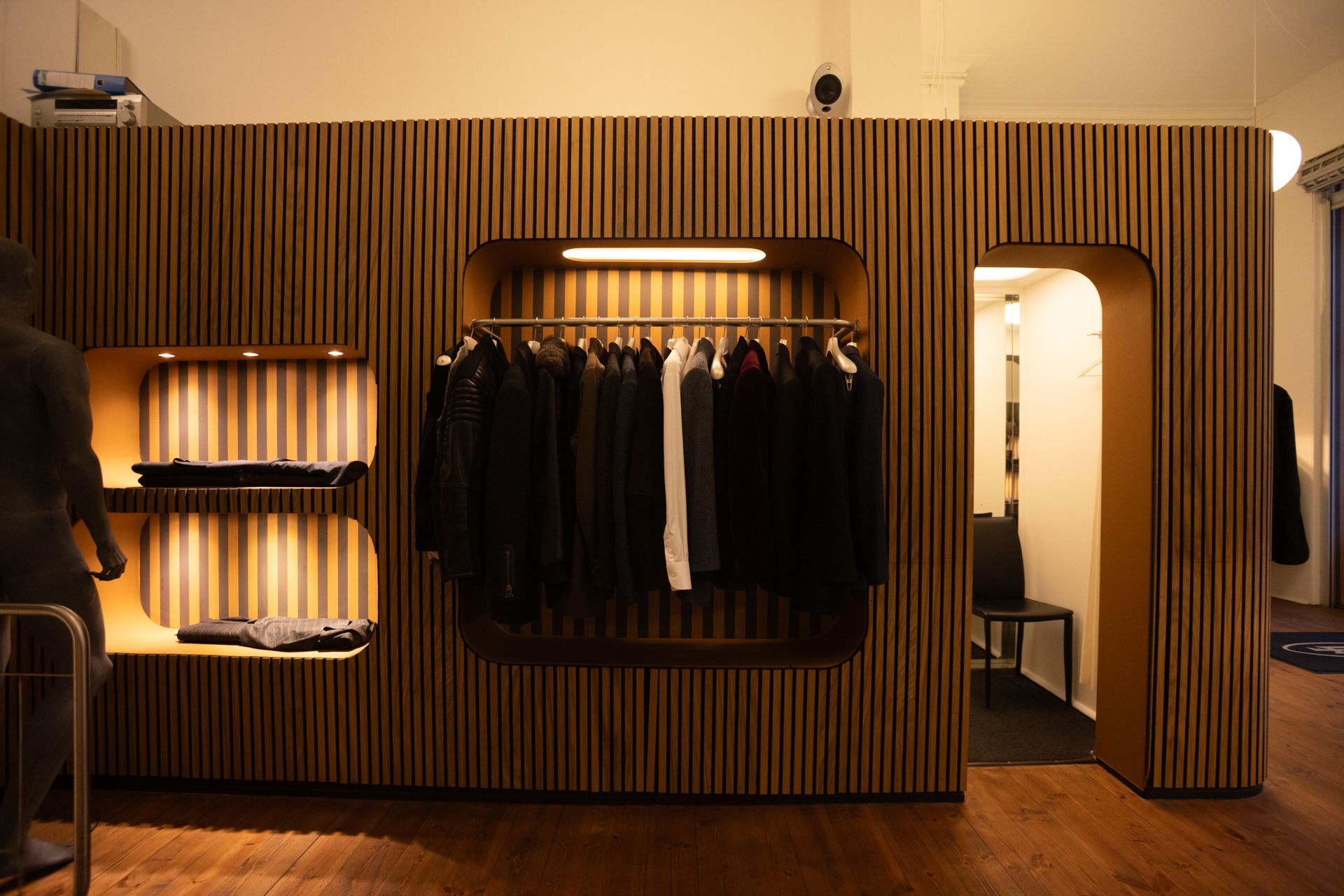 Lejemaglig butik med elegant tøjskab, spejl og åbne døre, placeret på Frederiksborggade i København. Væggene er dekoreret med lyse og mørke striber og indeholder flere hylder og opbevaringsrum.