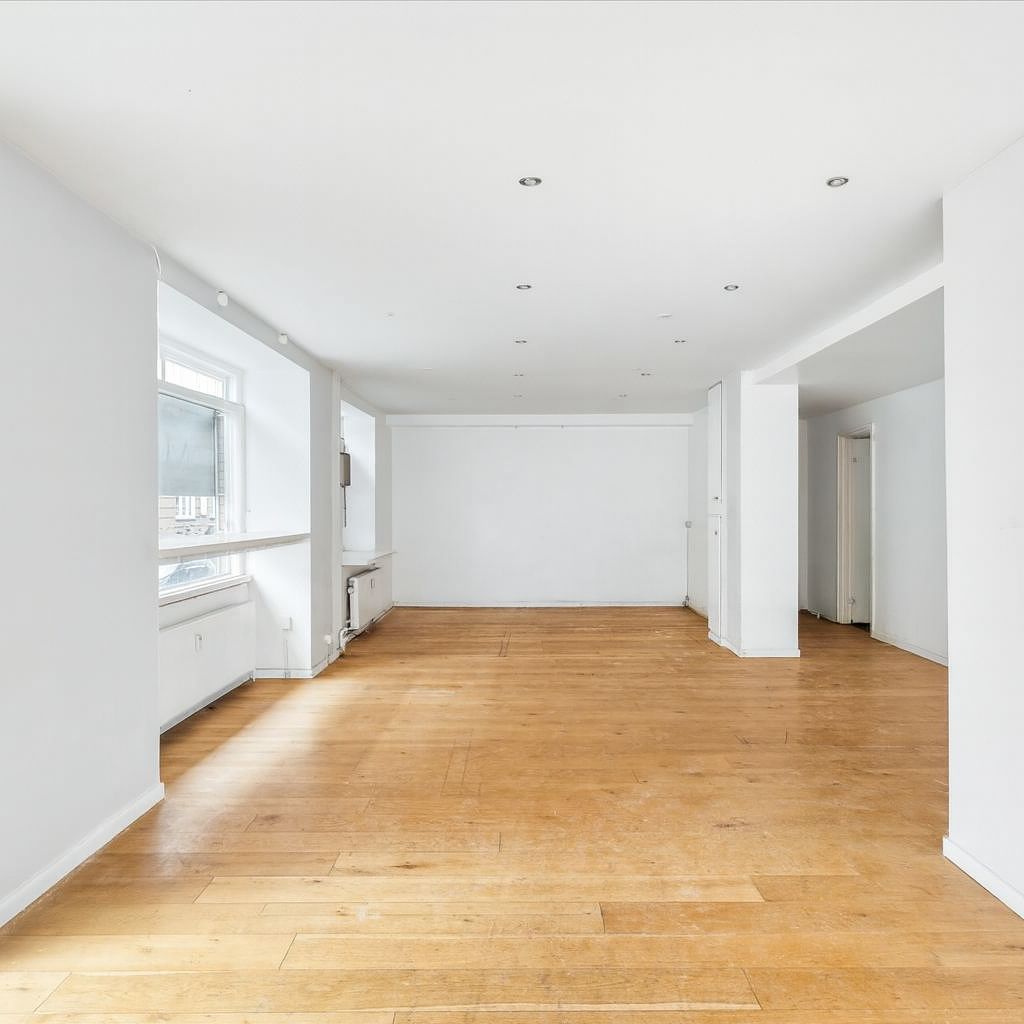 Erhvervslejemål med store vinduer og hjørnefacade, hvid væg og trægulv