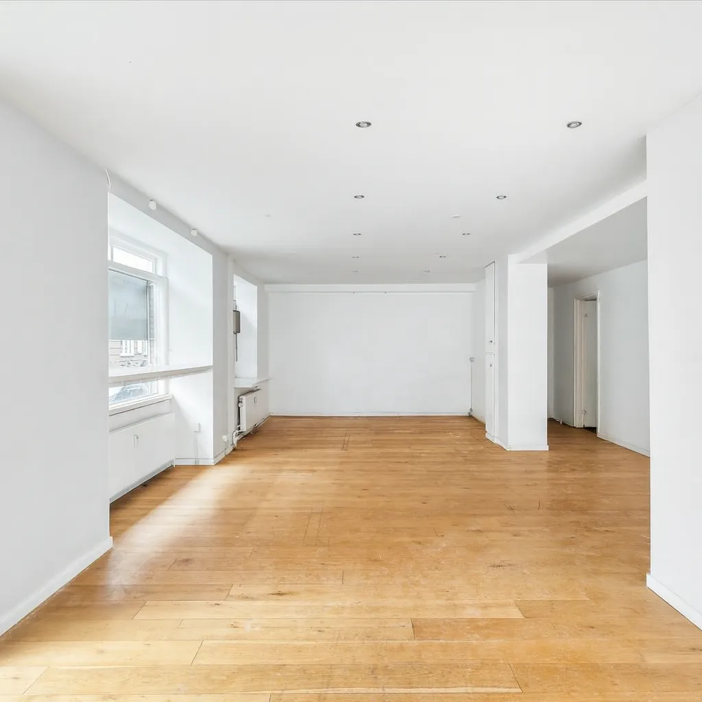 Erhvervslejemål med store vinduer og hjørnefacade, hvid væg og trægulv