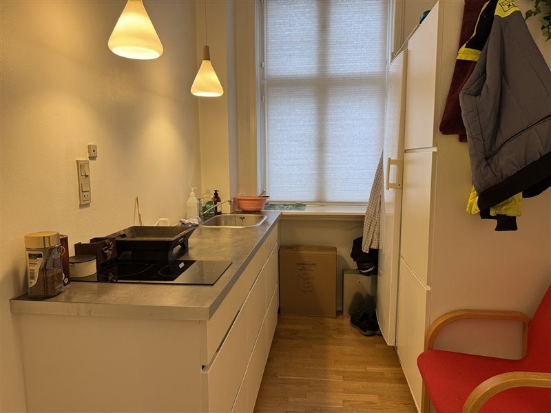 Moderne kontor med køkken og spiseplads. Hvidt køkken med gaskomfur og lysekroner. Seng og kufferter i kælderen.