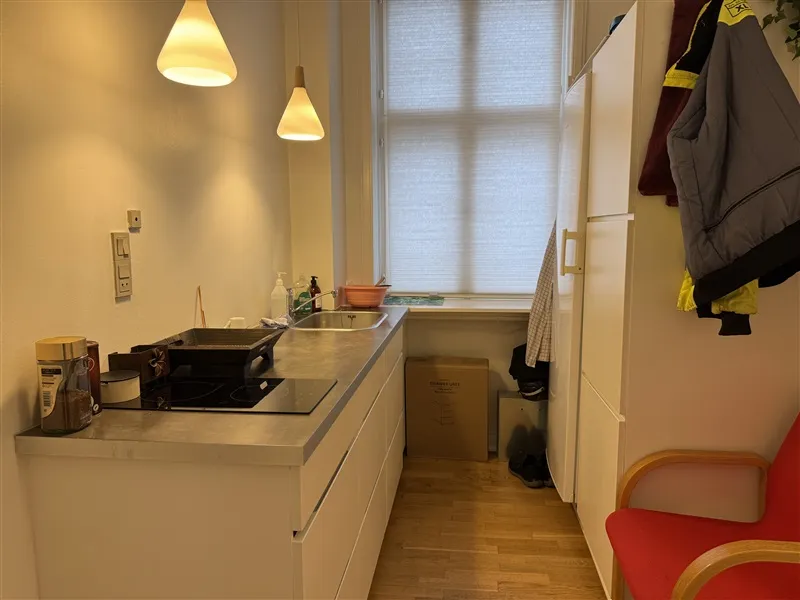 Moderne kontor med køkken og spiseplads. Hvidt køkken med gaskomfur og lysekroner. Seng og kufferter i kælderen.