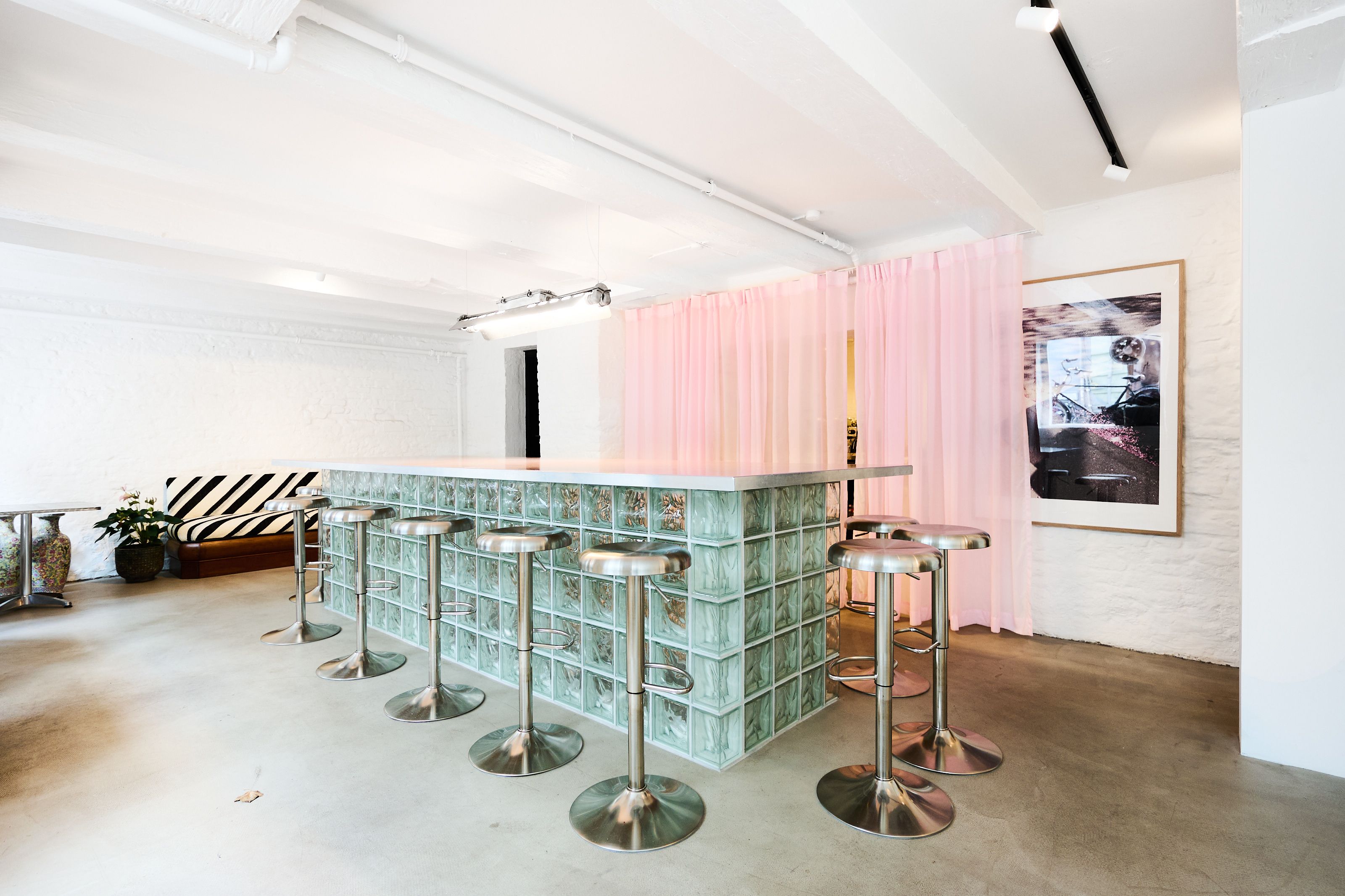 Investeringsejerlejlighed med køkken med moderne glasmuren, lysekroner, høje stole, pink gardiner, kunstværk og møbler i hjørnet