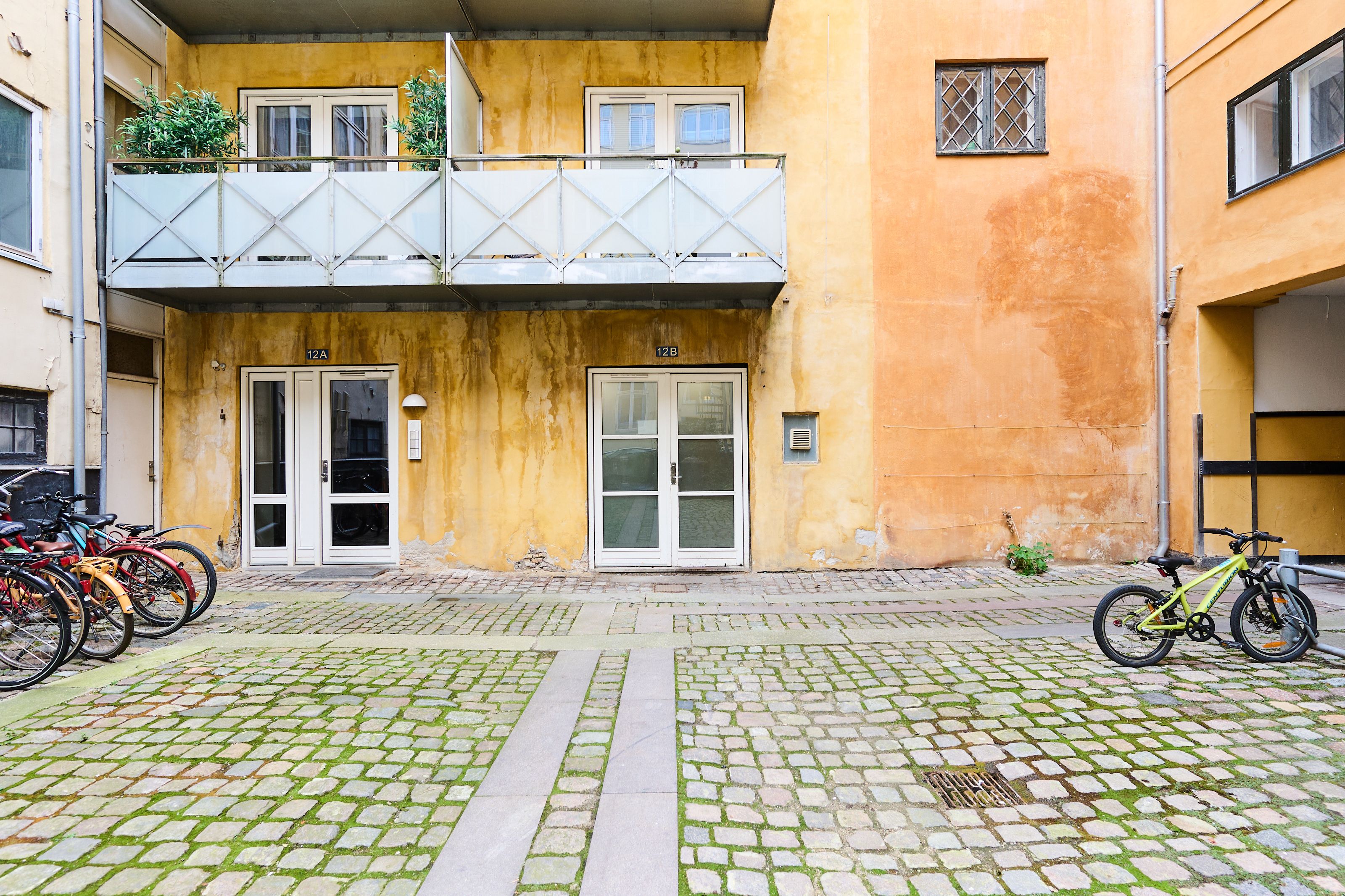 Lejlighed i Frederiksstaden til salg med parkerede cykler, gamle byggede gule vægge og højtliggende balkon med plantepot.