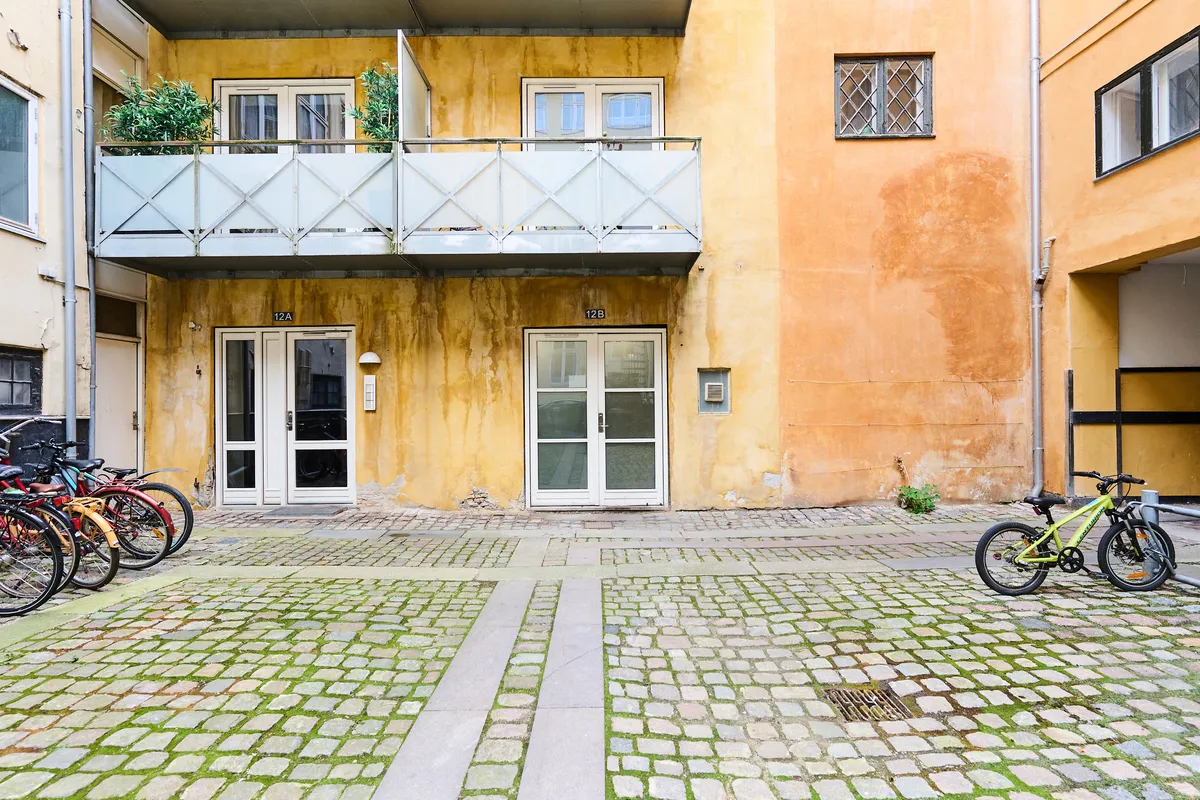 Lejlighed i Frederiksstaden til salg med parkerede cykler, gamle byggede gule vægge og højtliggende balkon med plantepot.