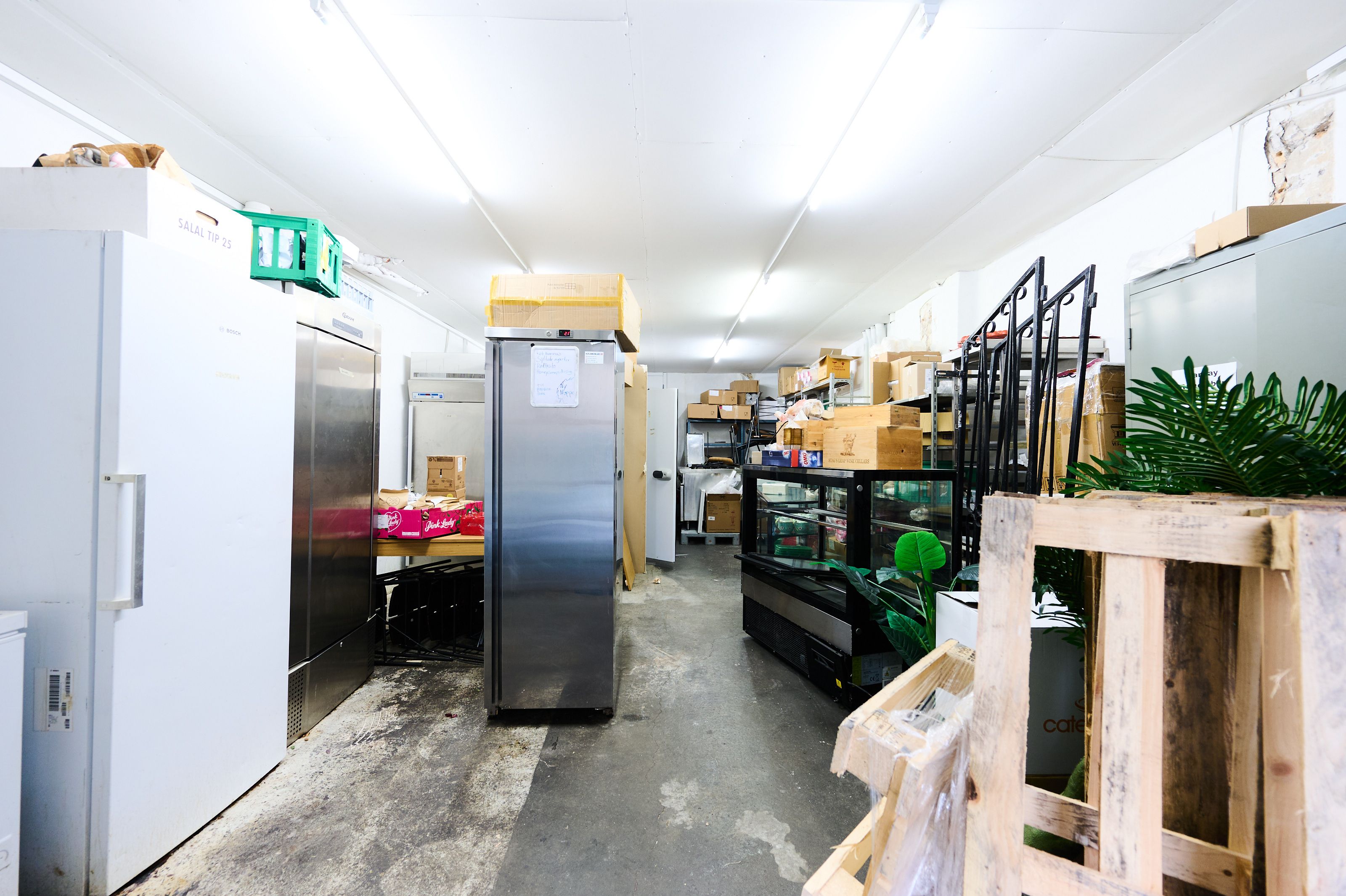 Investeringsejerlejlighed i Frederiksstaden, med køleskabe og lagerrum. Mange kasser og fragtpaletter. Væggene er hvide og lyse.
