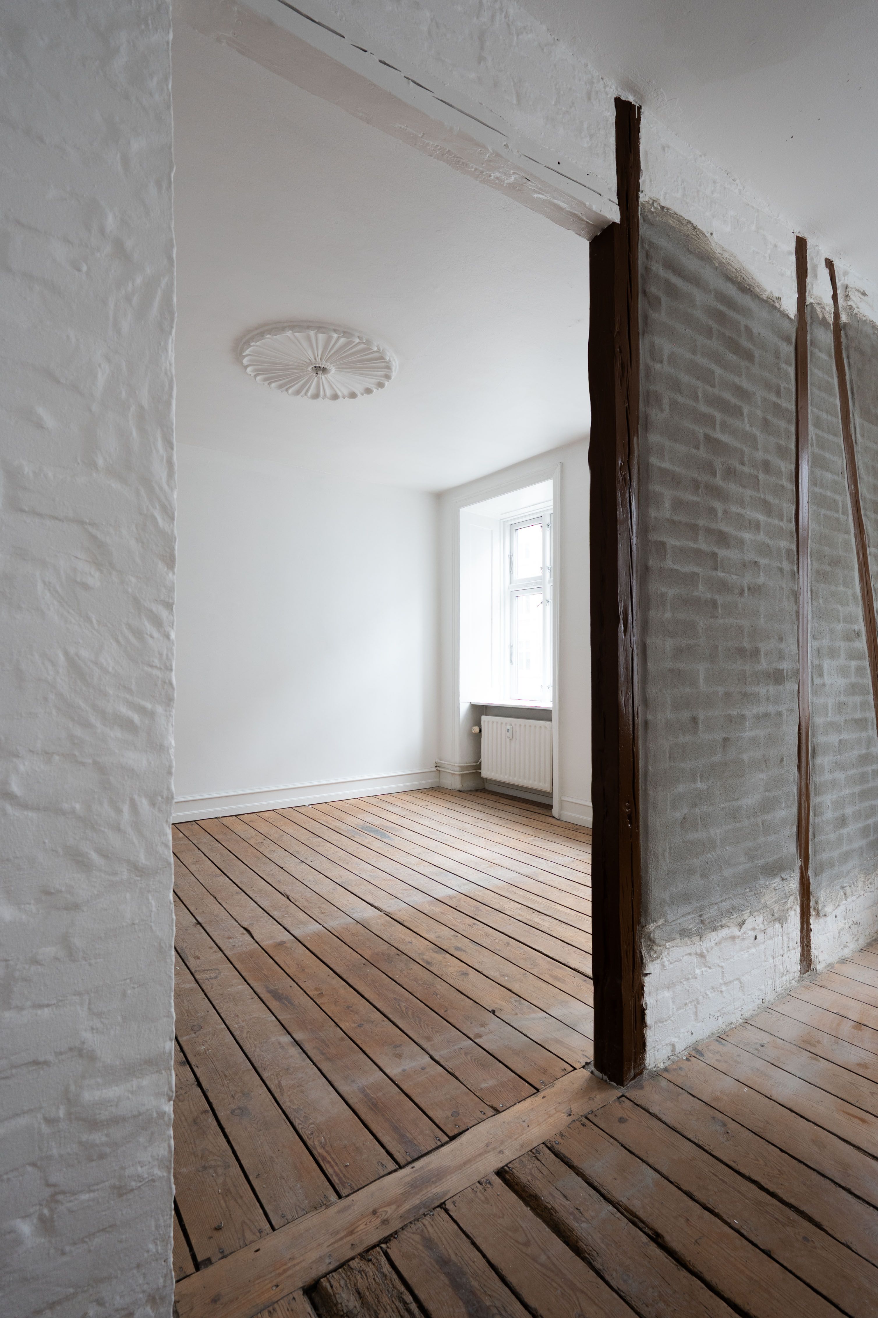 Et tomt rum med hvide vægge, gulv og loft samt et vindue og en radiator i rummet