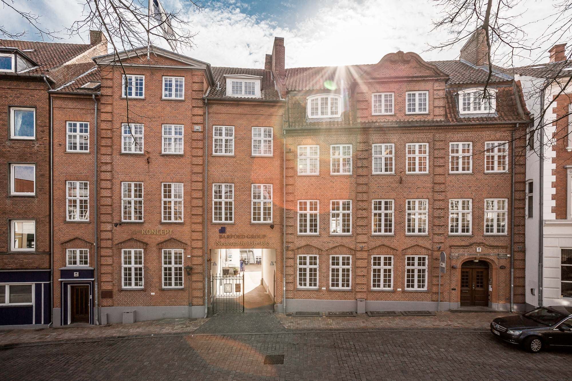 Kontor til leje på Nedergade 33, 1., 5000 Odense C. En flot bygning med røde mursten og flere vinduer. Der er parkeret en sort bil foran.