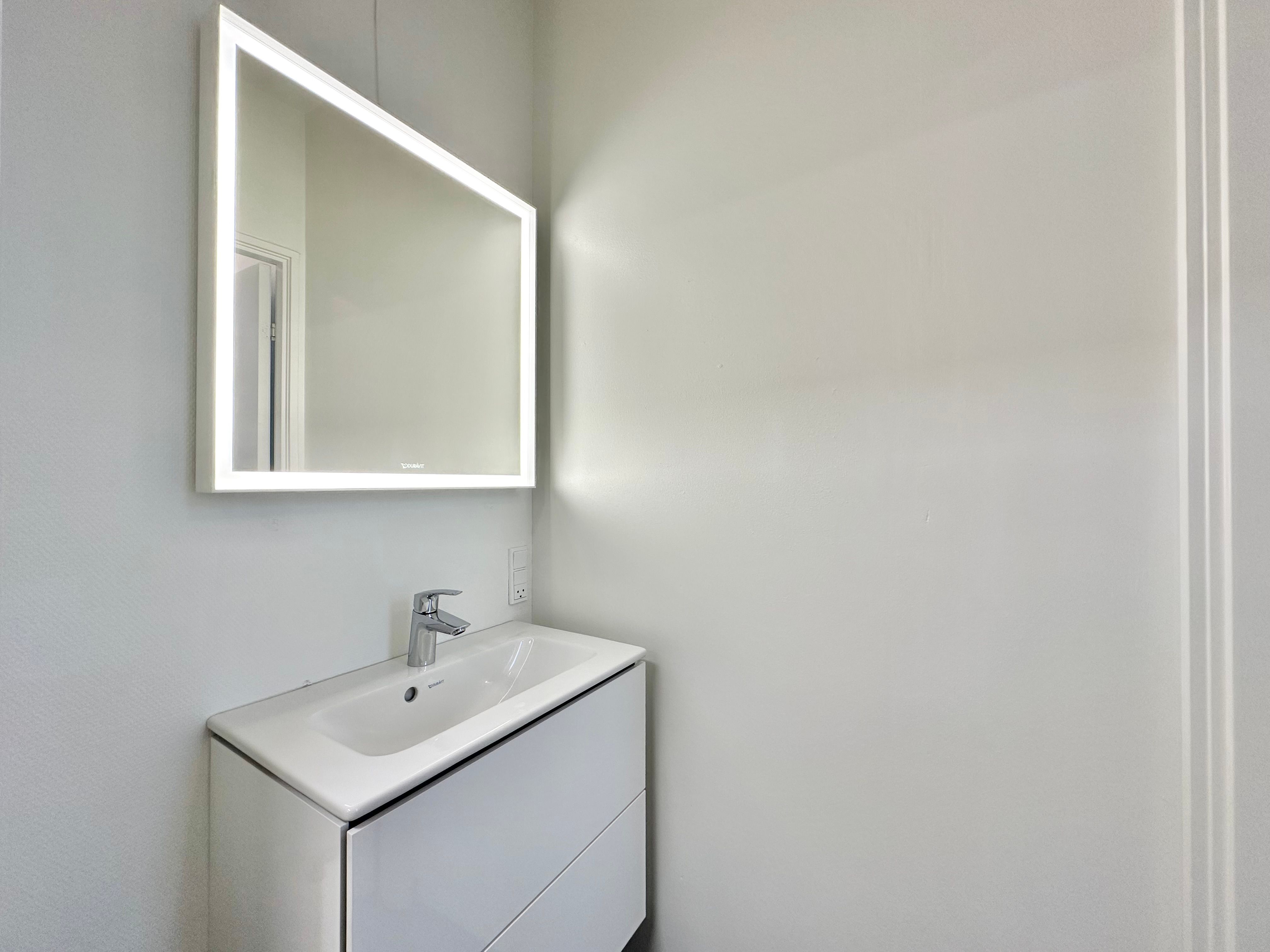 Nyd et moderne og rent badeværelse med en hvid spejlskab og en simpel, hvid vask med en enkelt vandhane