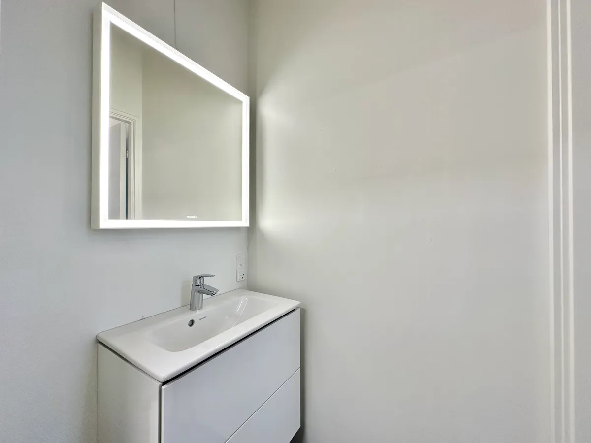Nyd et moderne og rent badeværelse med en hvid spejlskab og en simpel, hvid vask med en enkelt vandhane