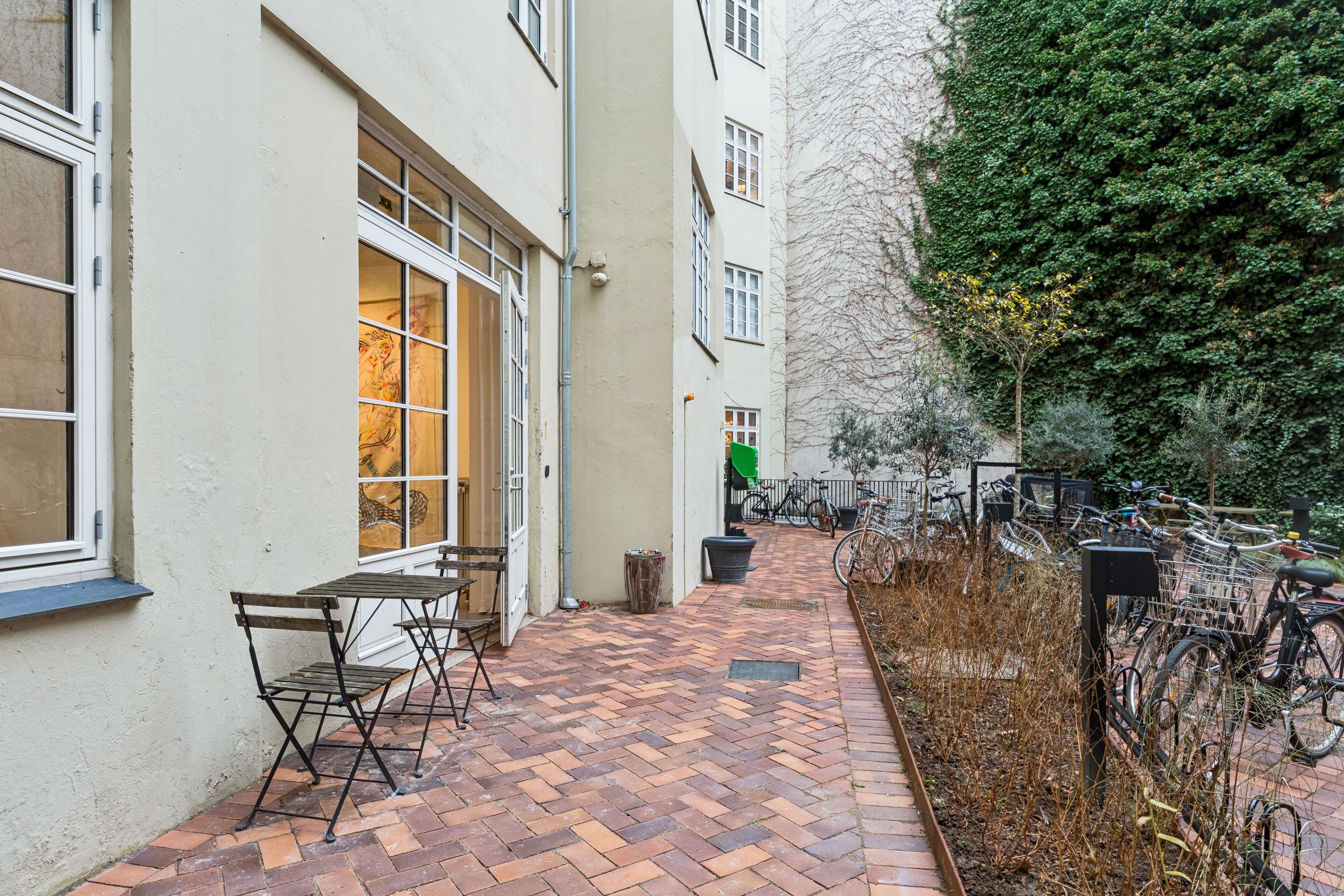 Butiksgård med terrasse og træbord og stole, hvor der er parkeret cykler langs gaden