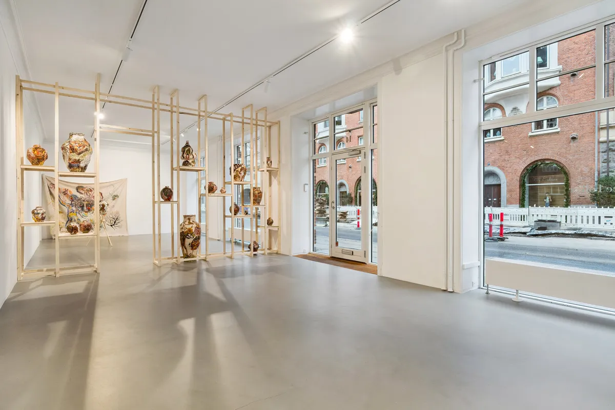 Store lyse vinduer, ren hvid væg og gulv, træhylder med keramik og kunstværker og en dør i midten