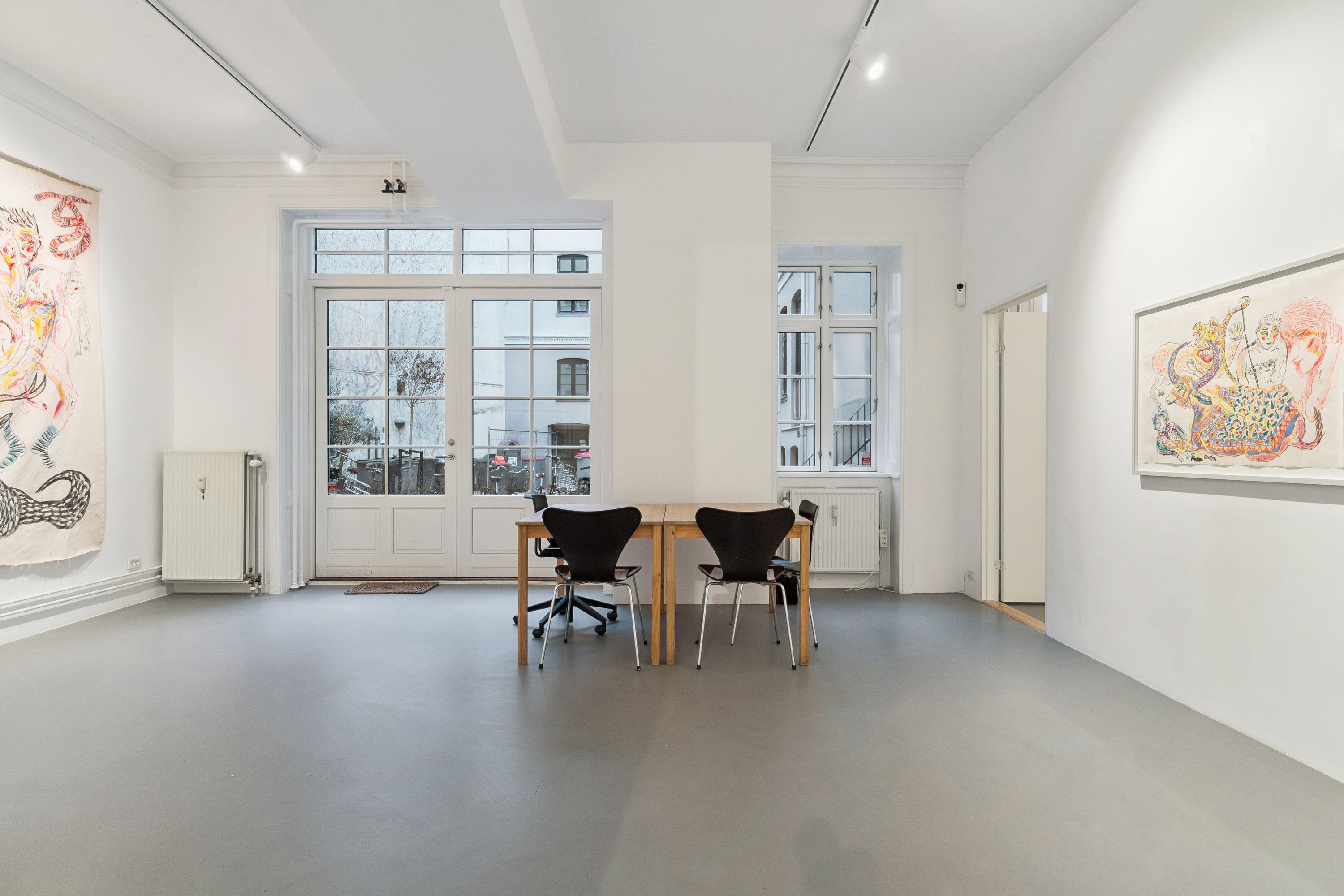 Et minimalistisk interiør med hvide vægge, lyse gulvbelægning, en stor træbord og lyse stolen, to store malerier og en radiator mod en væg