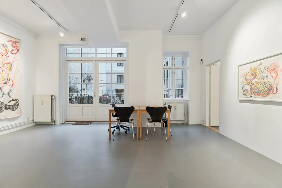 Et minimalistisk interiør med hvide vægge, lyse gulvbelægning, en stor træbord og lyse stolen, to store malerier og en radiator mod en væg